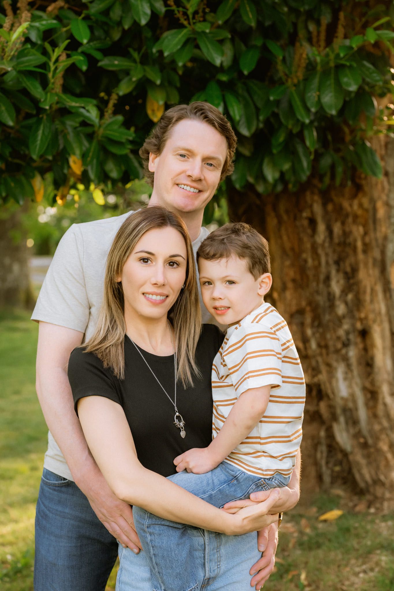 Family portrait pictures in front of a big tree, parents and their son hugging close