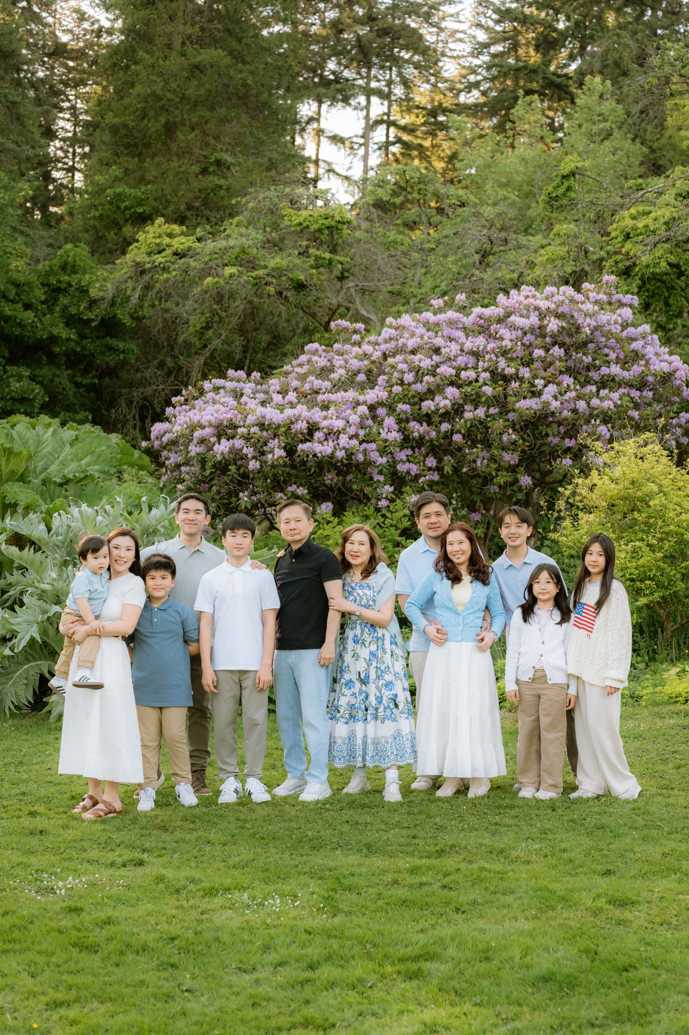 Professional family photoshoot, large family in blue and white standing in front of blooming purple rhododendrons