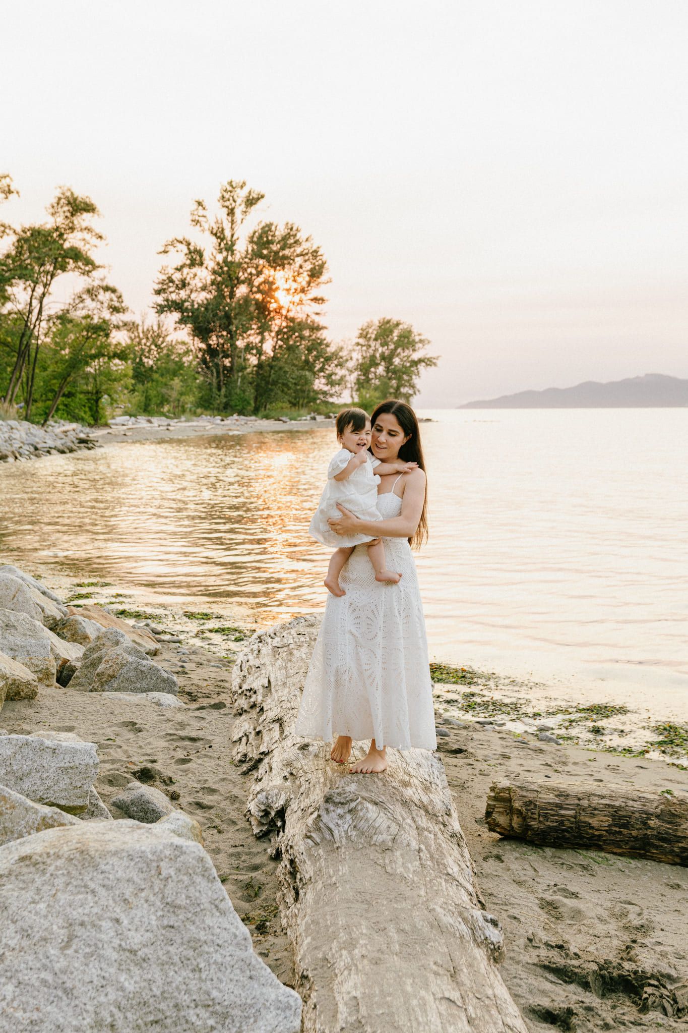 Mother holding her baby on a driftwood log at the edge of the sea