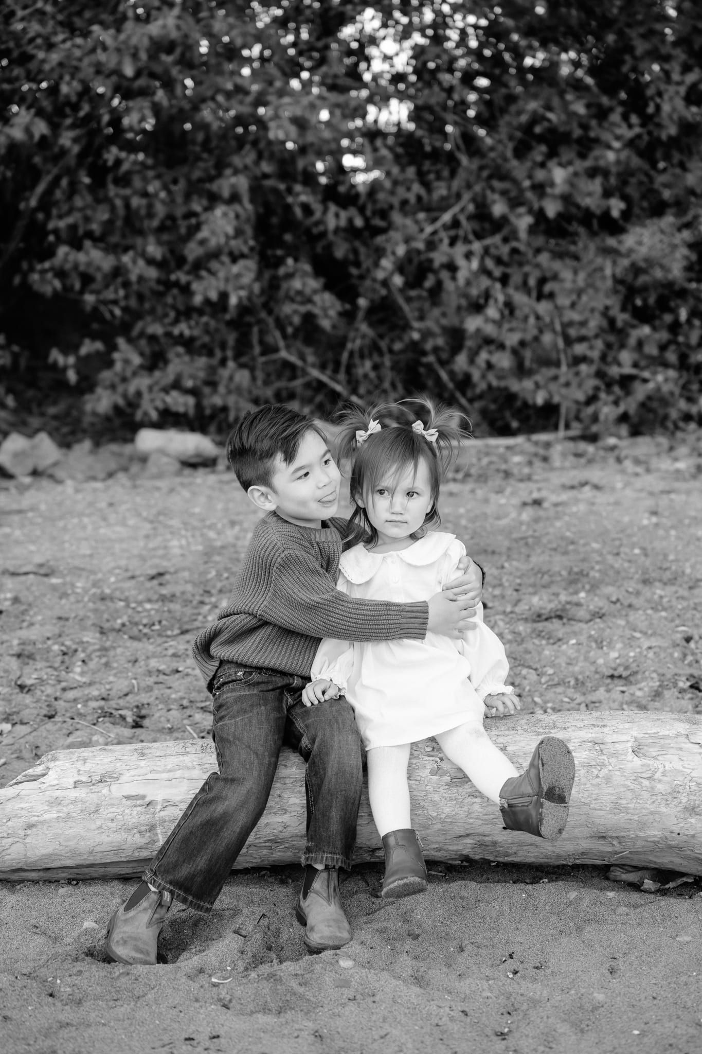 Black and white family photos on a driftwood log, a boy hugging his little sister