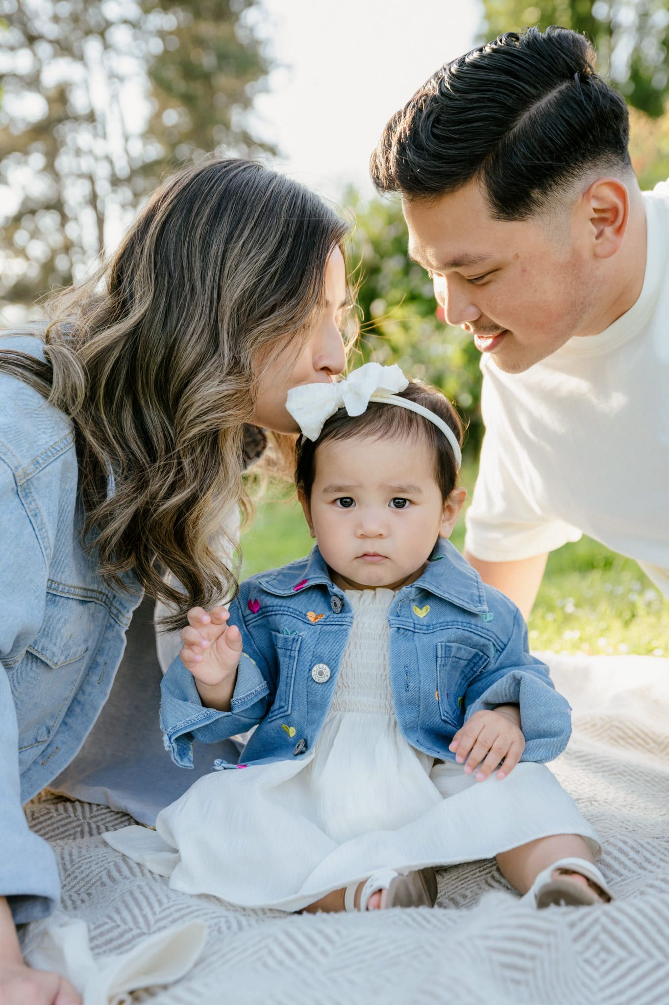 Creative family photography, mother and father leaning in close to their baby girl in a denim jacket and bow