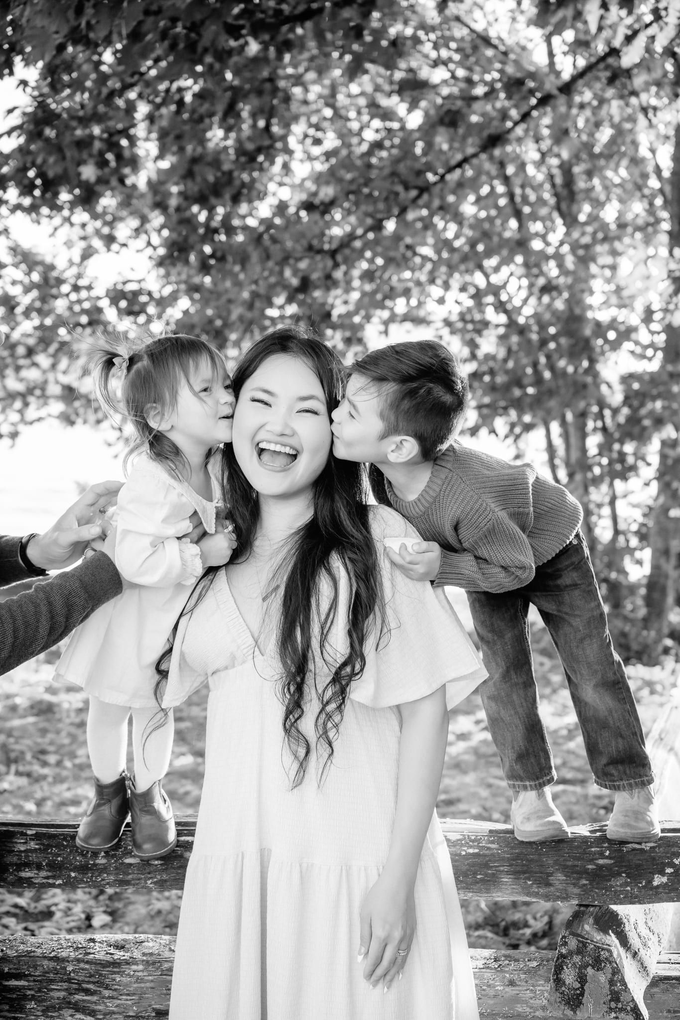 Fun family photo of two kids kissing their laughing mom on the cheeks, in black and white