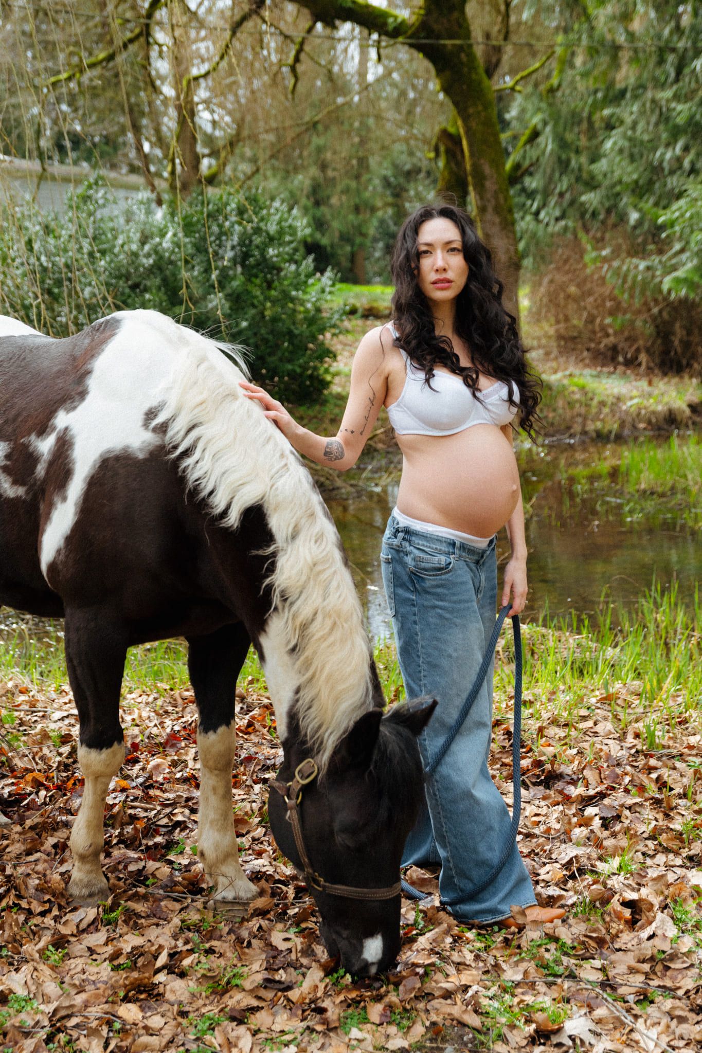 Creative maternity photography on a farm, expectant mother in a denim jacket with horses