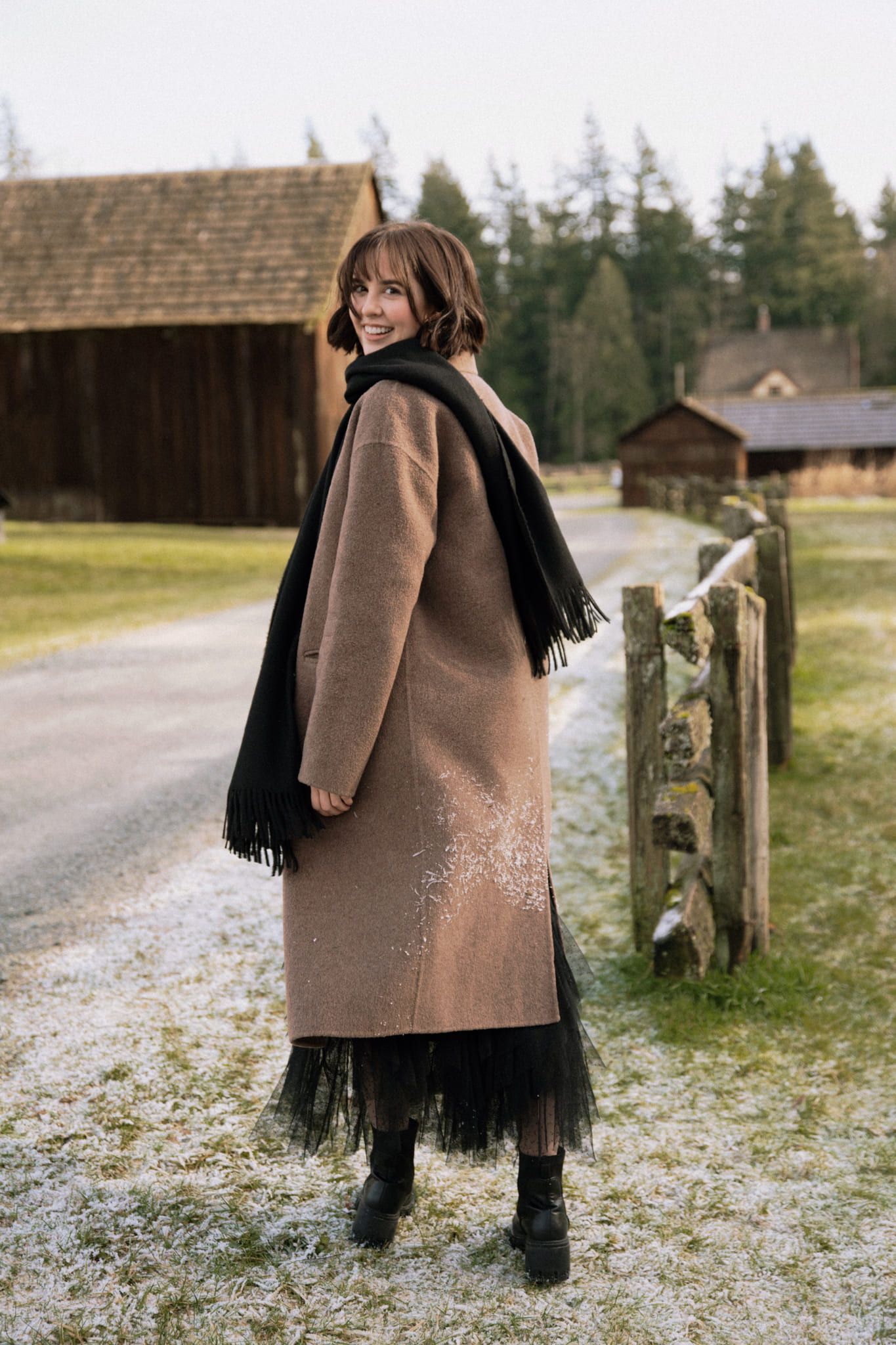 Portrait sessions at a heritage farm, woman in a long coat by a wooden fence