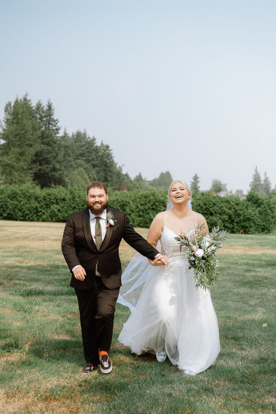 Candid wedding photography across a grassy field, bride and groom laughing as they walk hand in hand