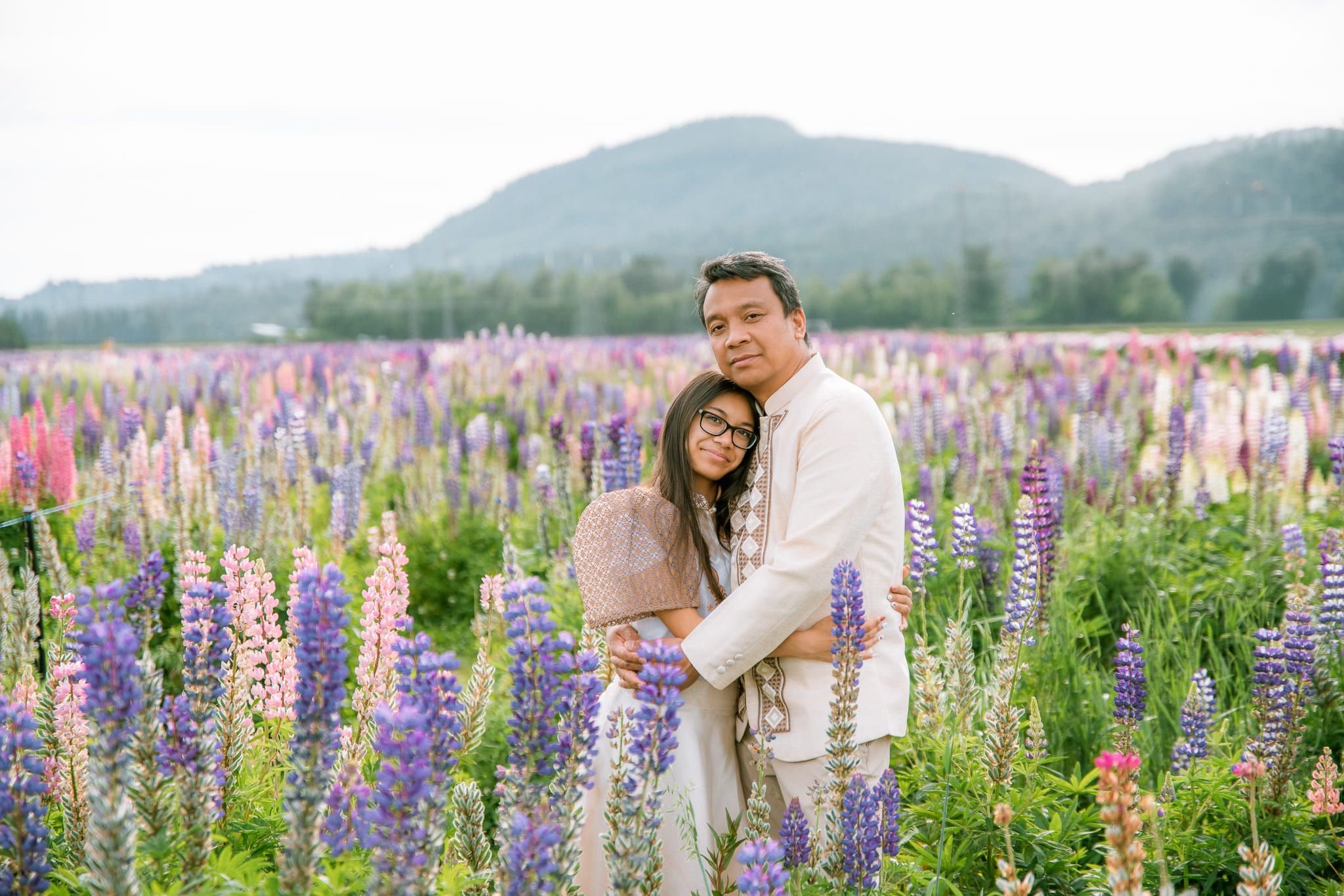 Couple embracing in a field of purple and pink lupins below the mountains