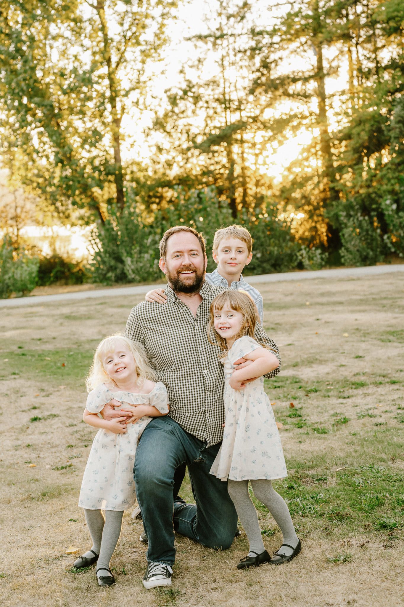 Family portrait photography in a sunny field, father kneeling with his three children