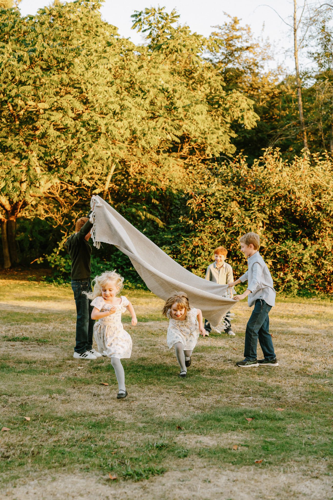 Candid family photo in a sunny field, children running under a blanket held up by their parents