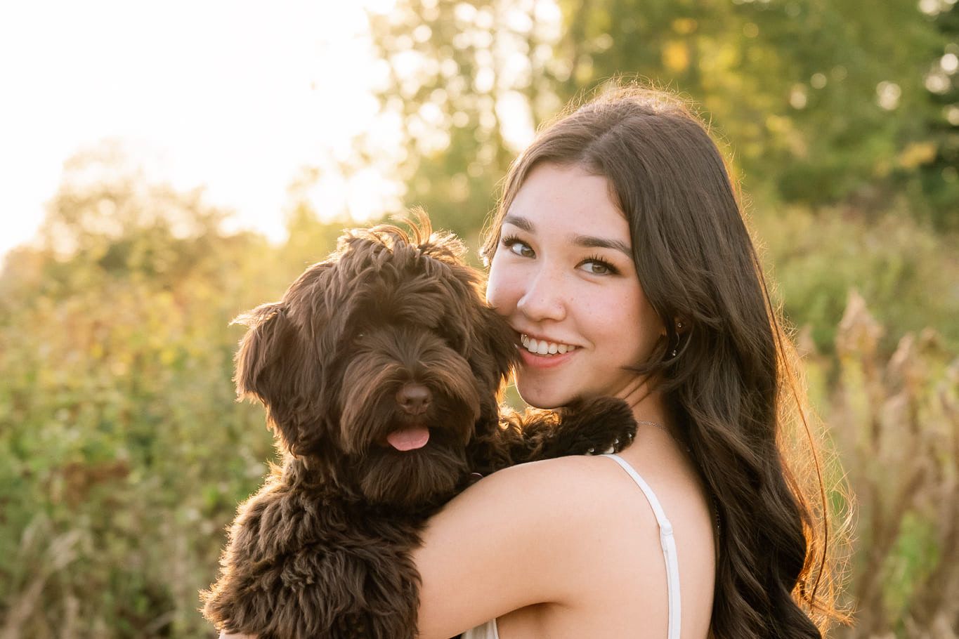 Outdoor portrait photography in a golden field, young woman hugging her curly brown dog