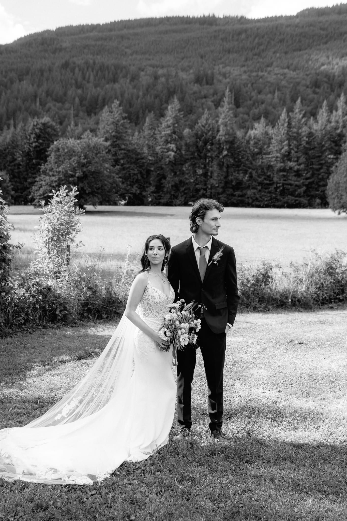 Black and white wedding photo of the bride and groom in a field below the hills