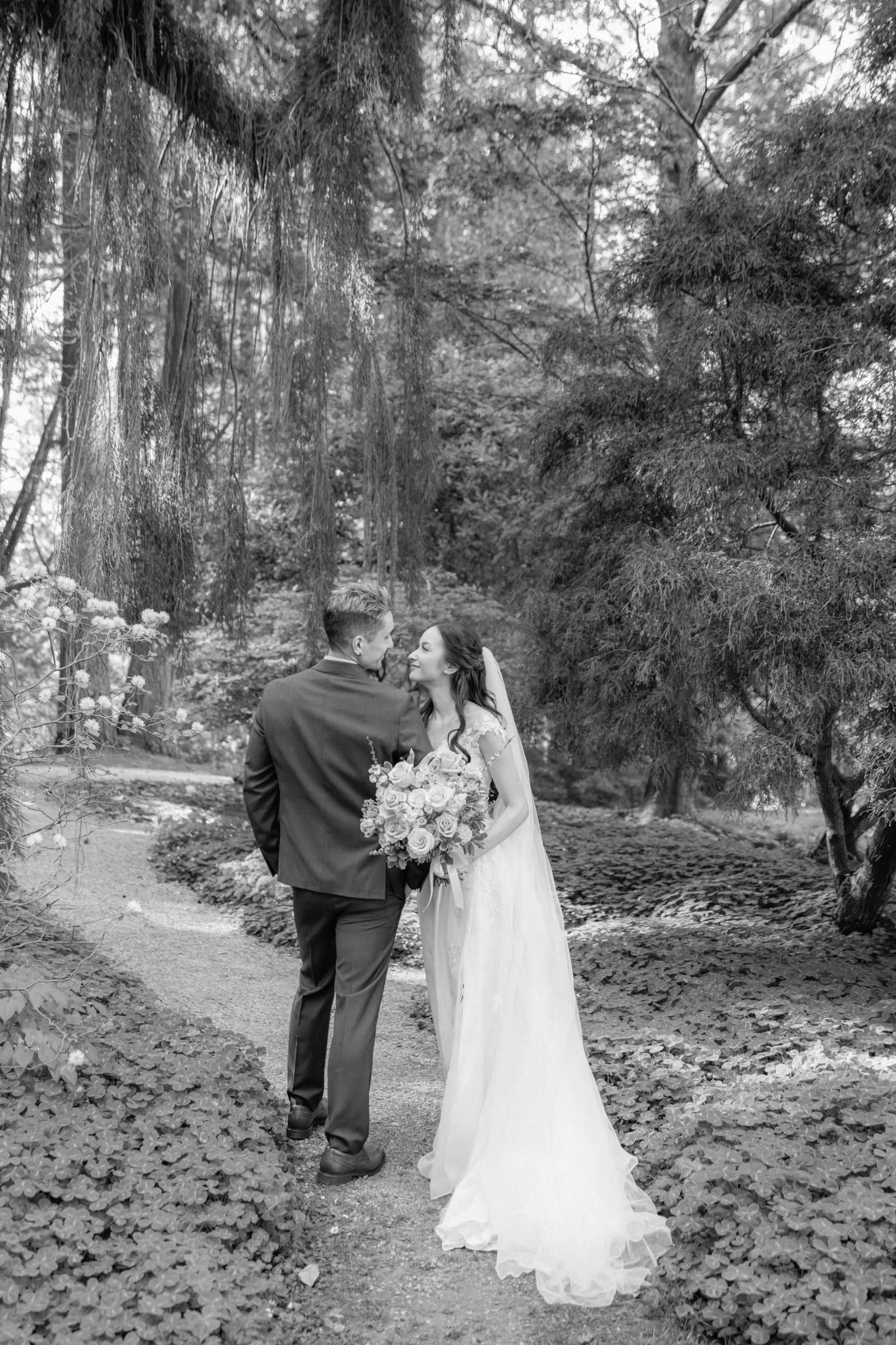 Black-and-white photo of the bride walking with her bouquet beneath the trees