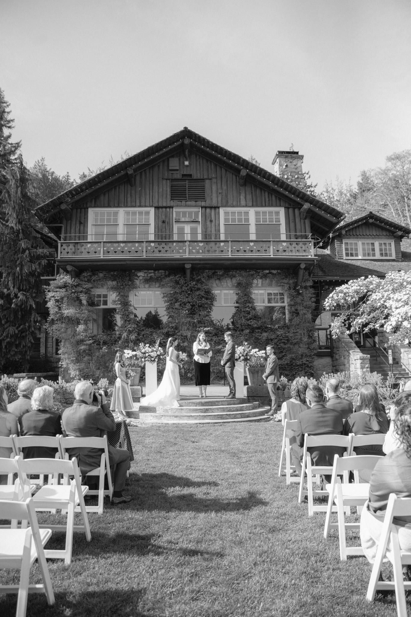 Black-and-white photo of guests seated before the stone lodge for the ceremony