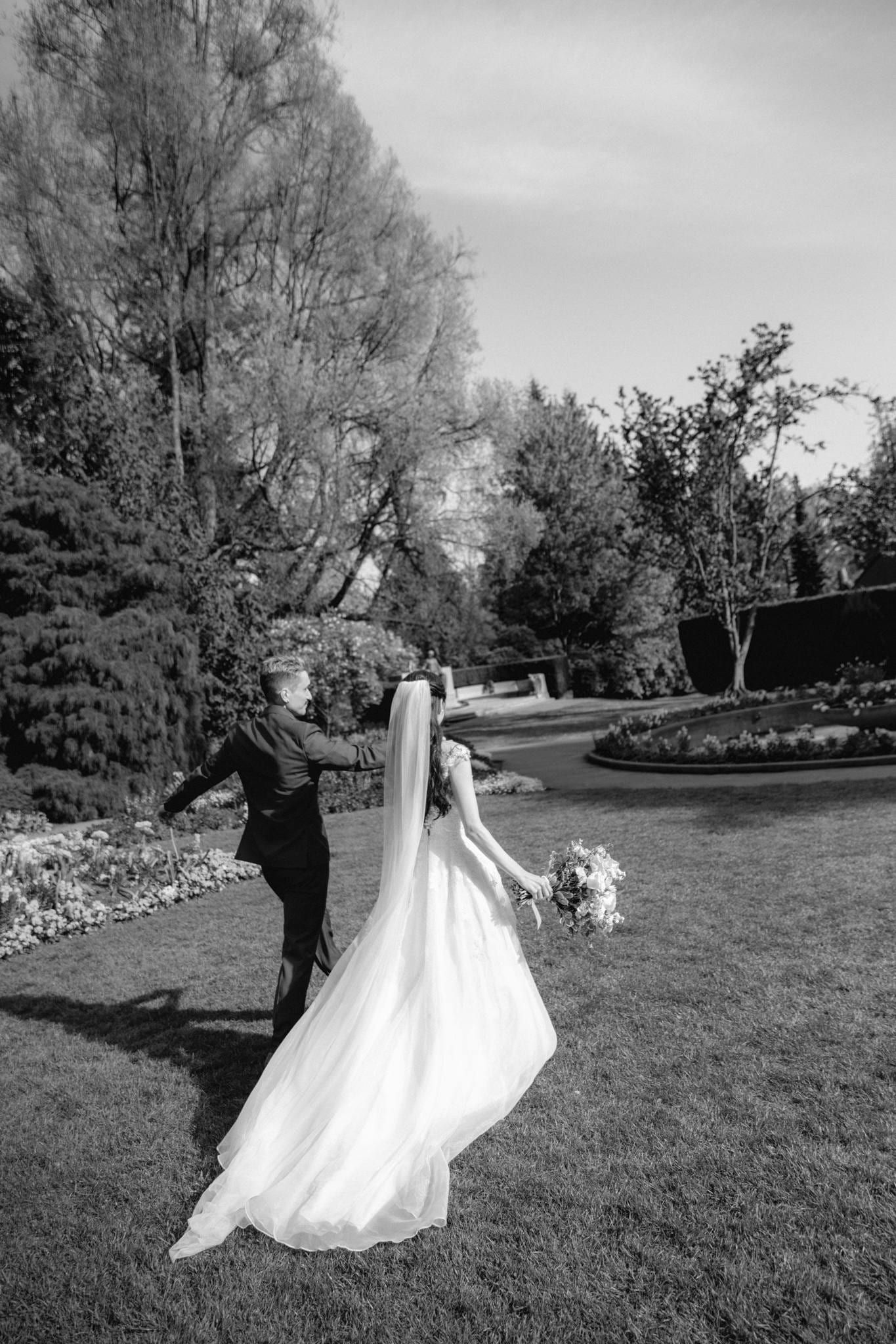Black-and-white photo of the bride walking through the garden, veil flowing