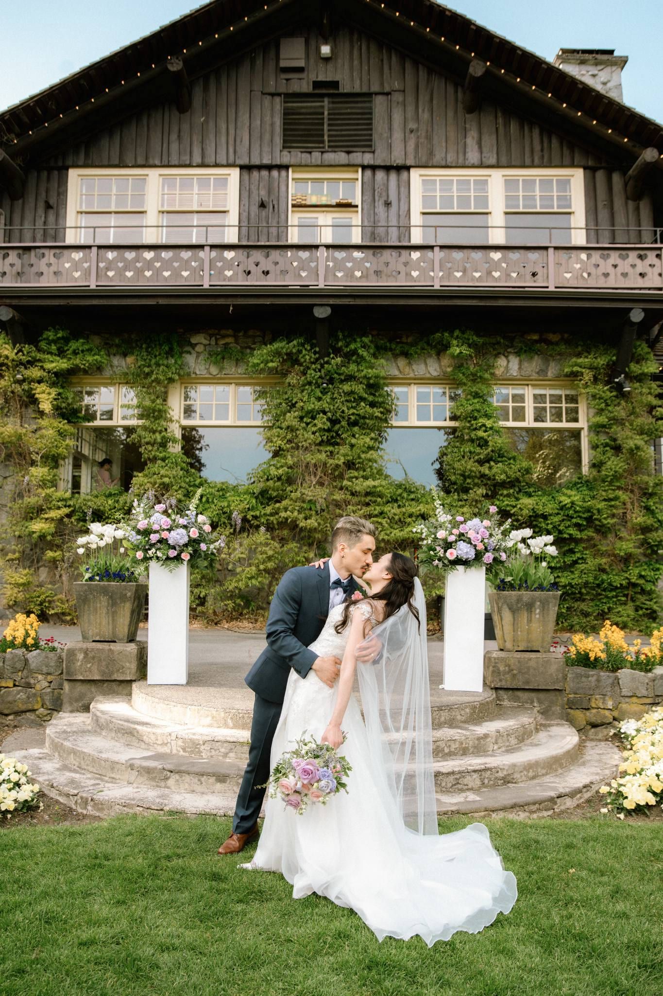 Newlyweds embracing before the stone lodge and its floral arch