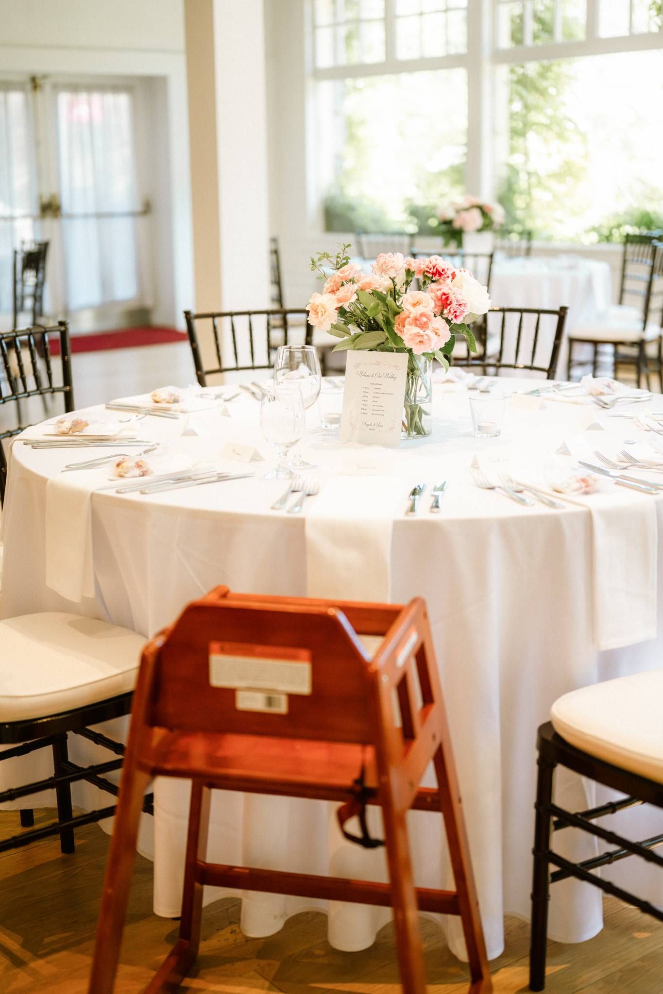 Reception table with a pink floral centrepiece and a red high chair