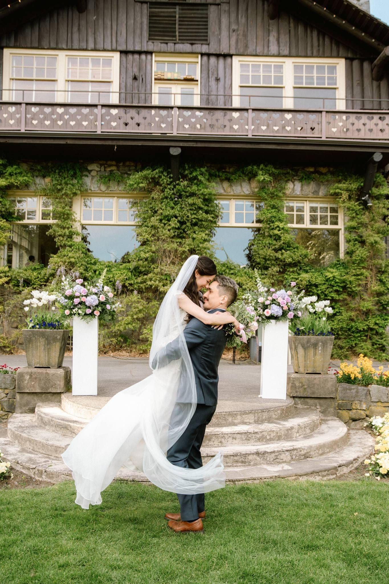 Groom lifting the bride beneath the floral arch before the lodge