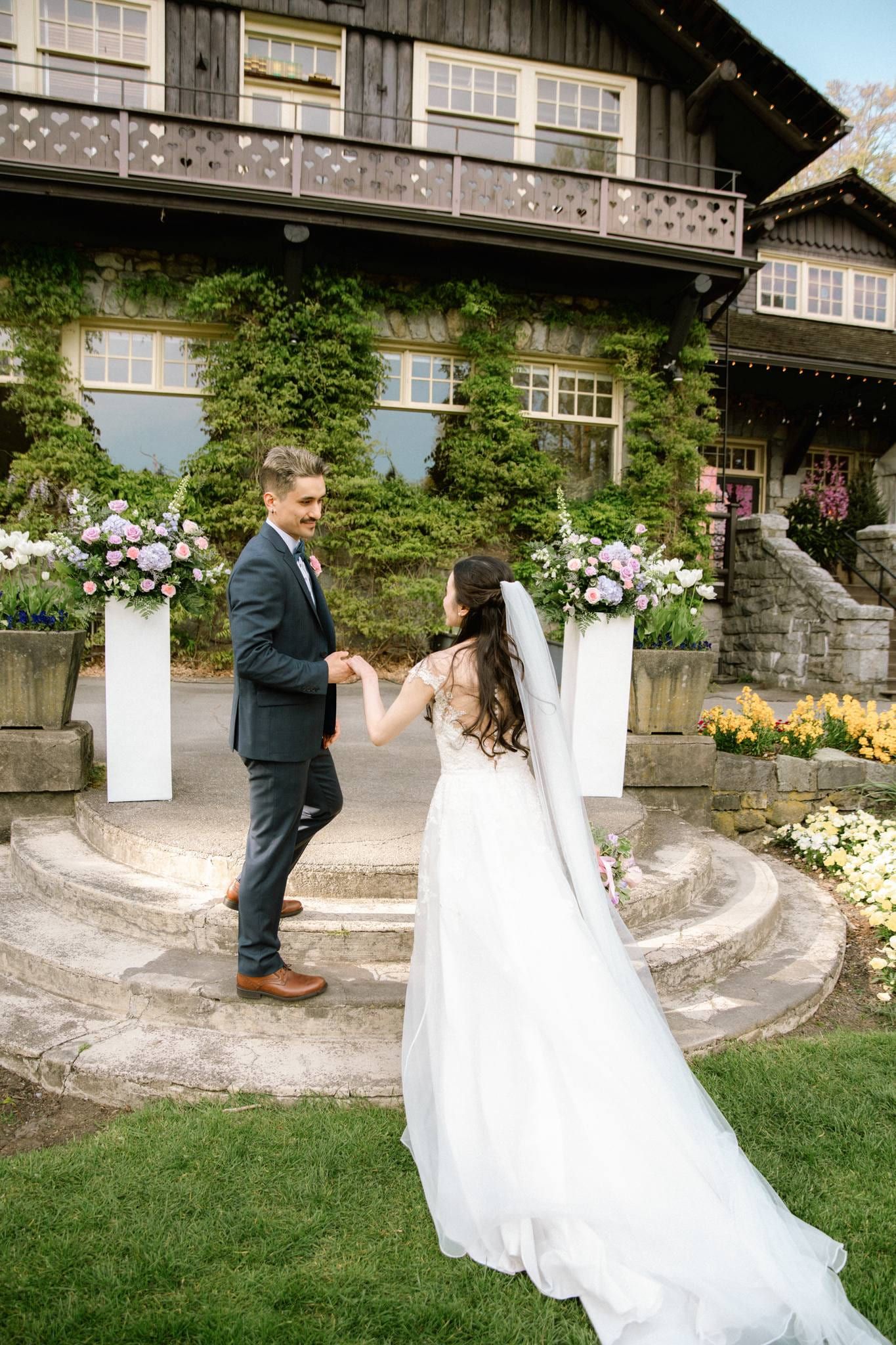 Couple holding hands before the stone lodge and its floral arch