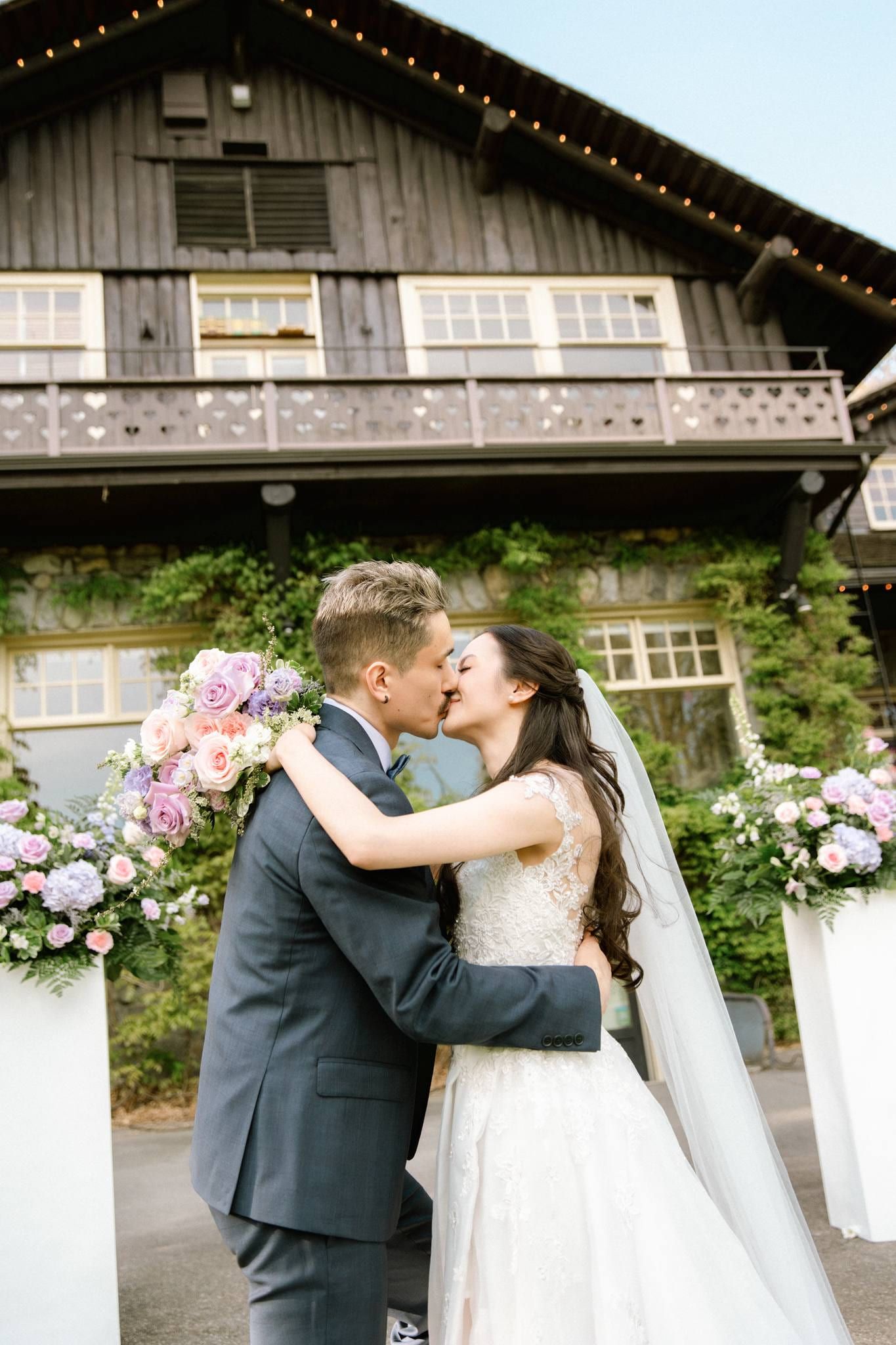 Groom kissing the bride's cheek beside the floral arch