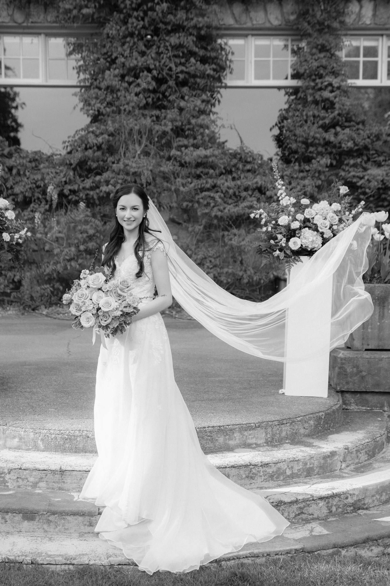 Black-and-white photo of the bride lifting her veil on the garden steps