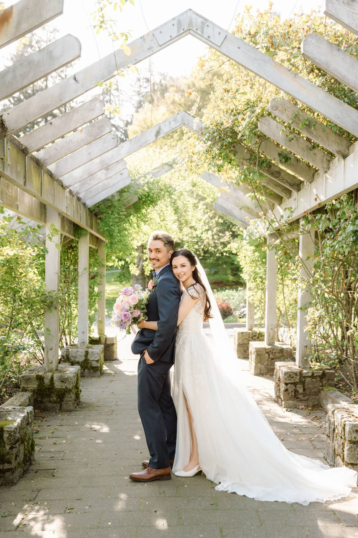 Bride and groom under the pergola with her veil trailing