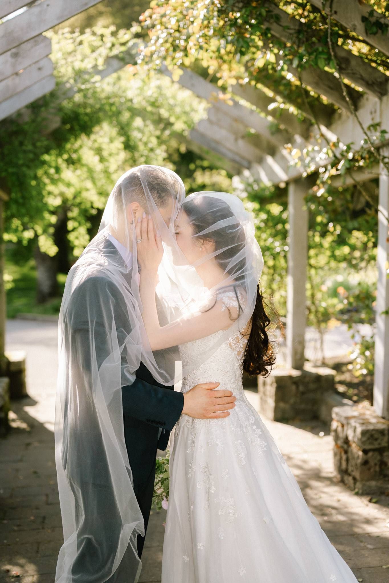 Couple kissing beneath the veil under the pergola