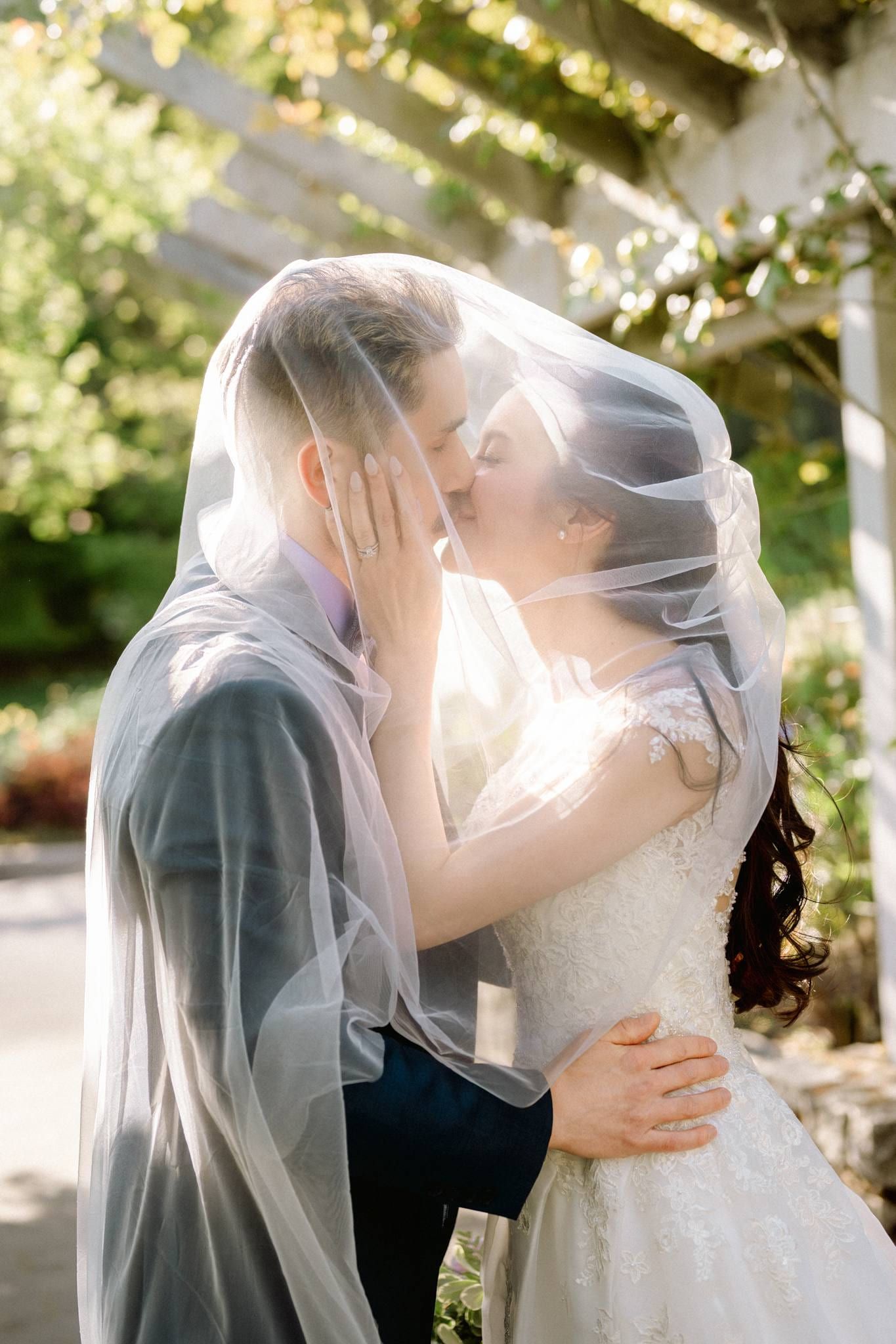 Couple kissing beneath the veil under the pergola