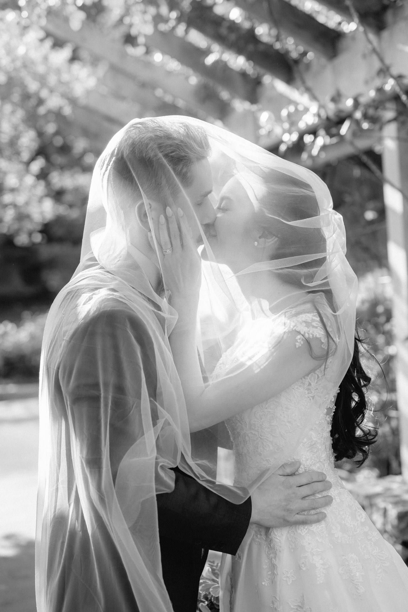 Black-and-white photo of the couple beneath the veil in dappled light