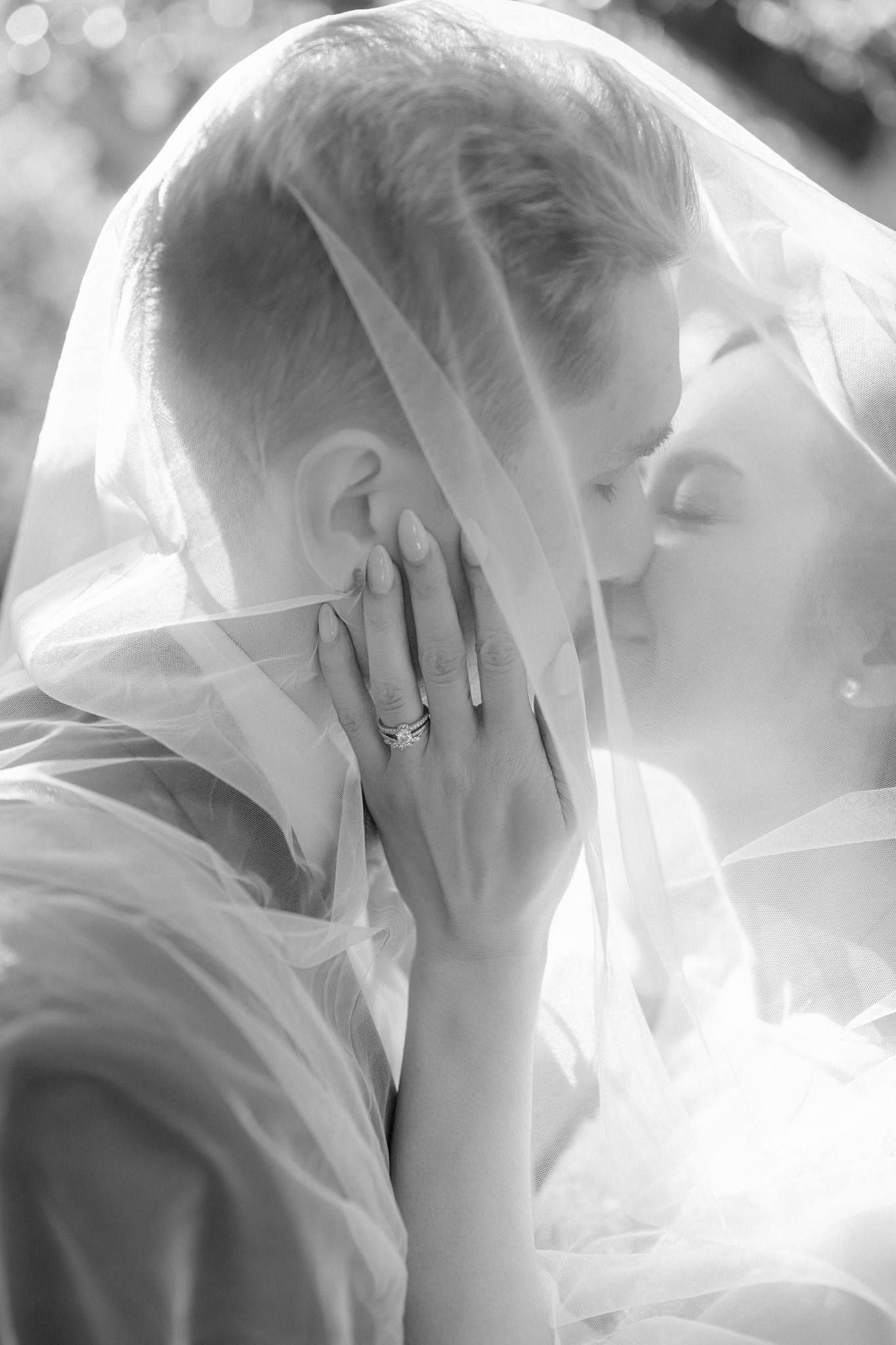 Bride and groom beneath her veil, foreheads together
