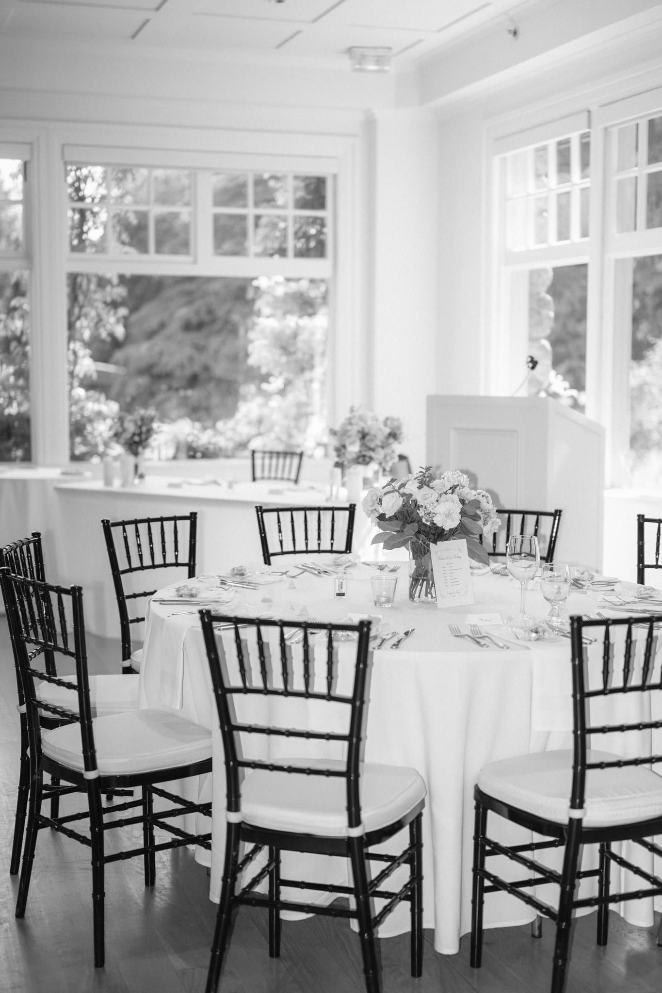 Reception tables set with white linen and dark chiavari chairs in the conservatory