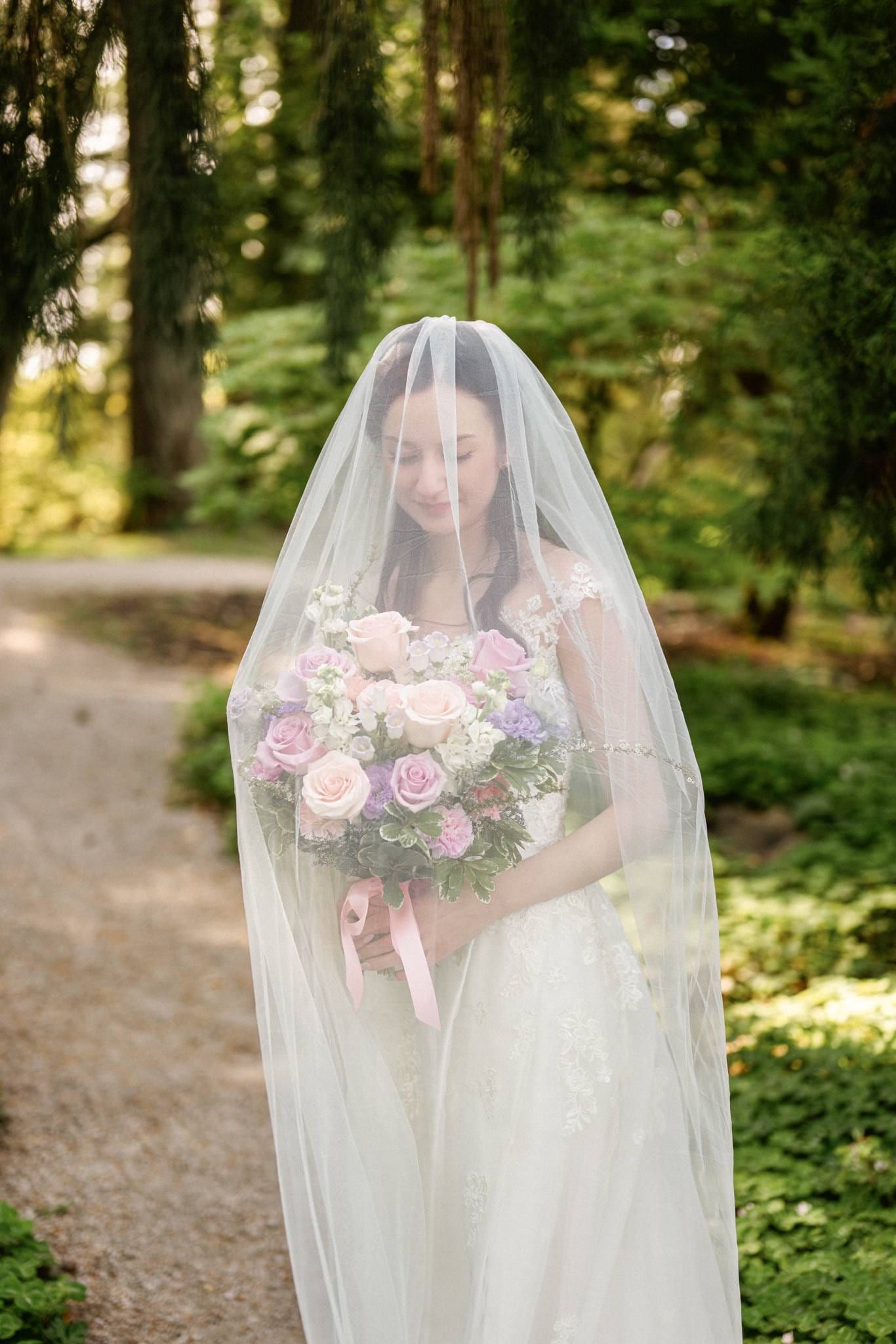 Bride beneath her veil holding a pastel bouquet in the garden