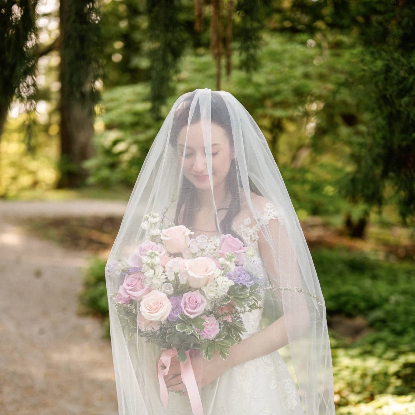 Angela beneath her veil holding a pastel bouquet in the garden