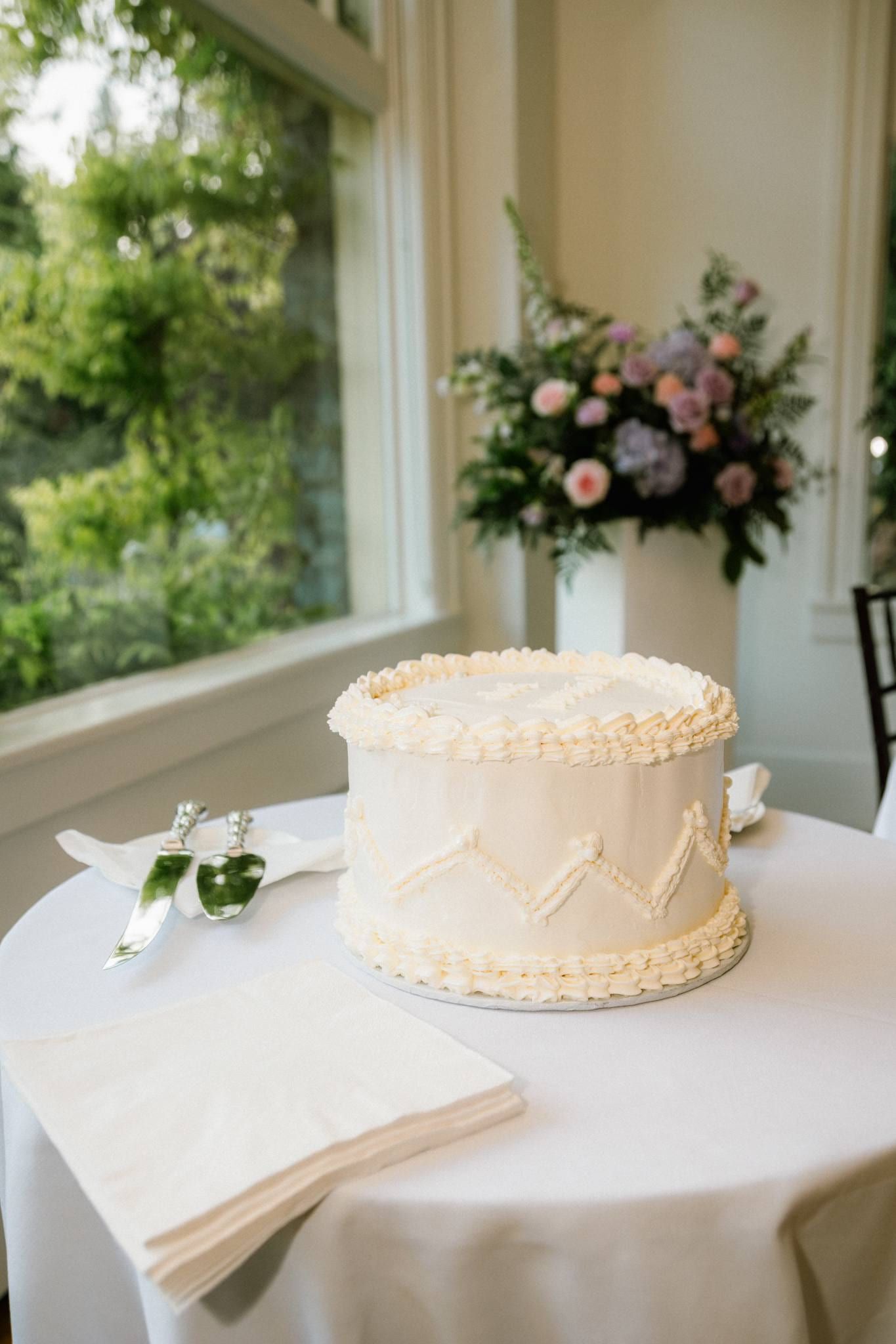White wedding cake beside a floral bouquet in the window