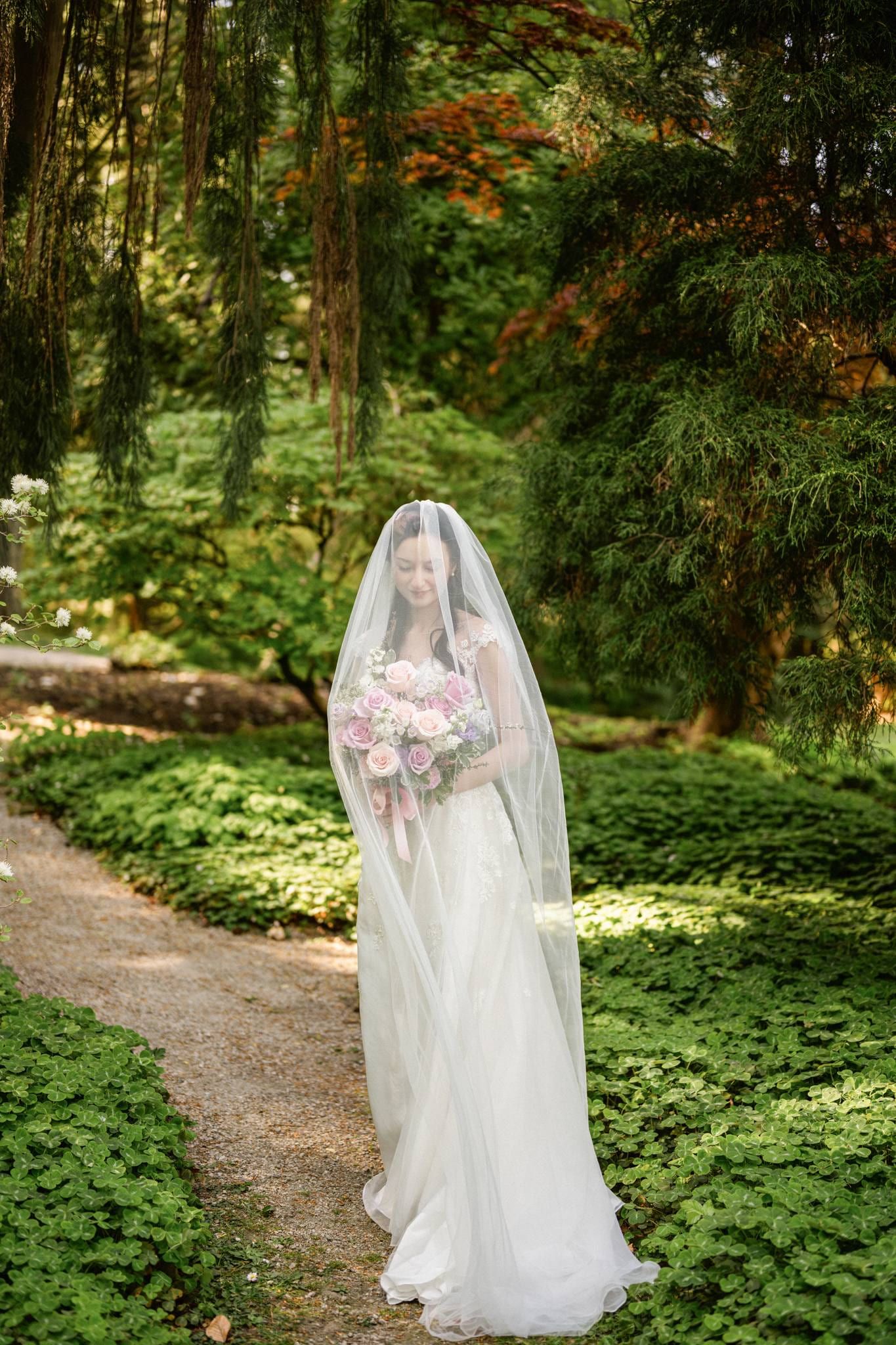 Bride under her veil walking the leafy garden path