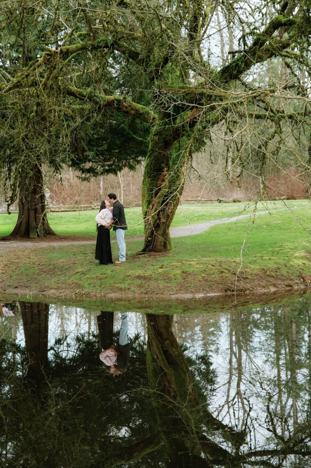Intimate couples photo, a couple kisses beneath mossy trees, reflected in a still pond