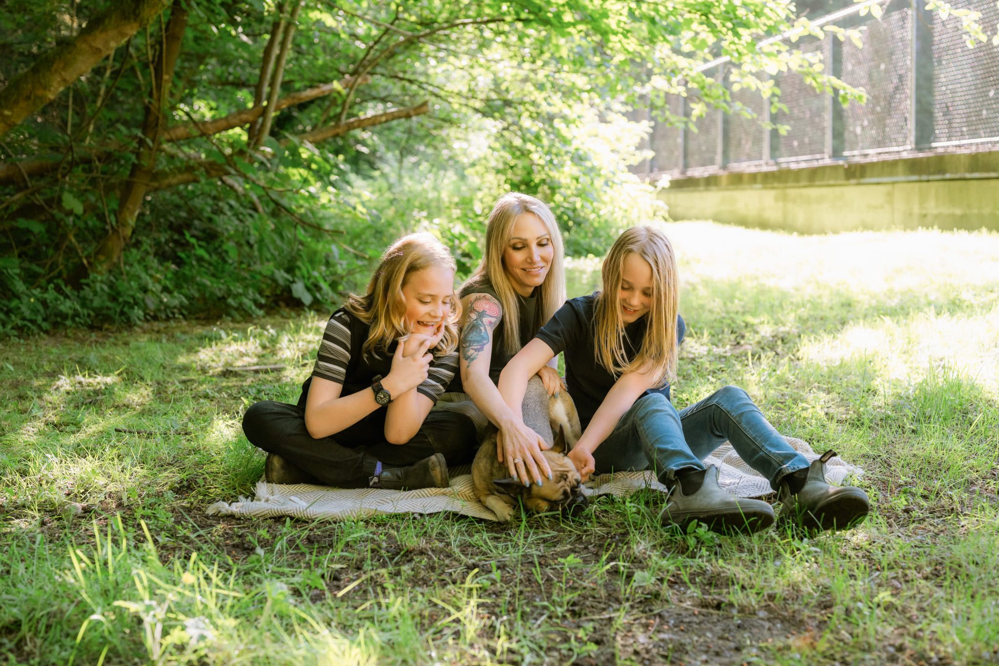 Family pet photography, mother and daughters sitting on a blanket in a forest clearing with their dog