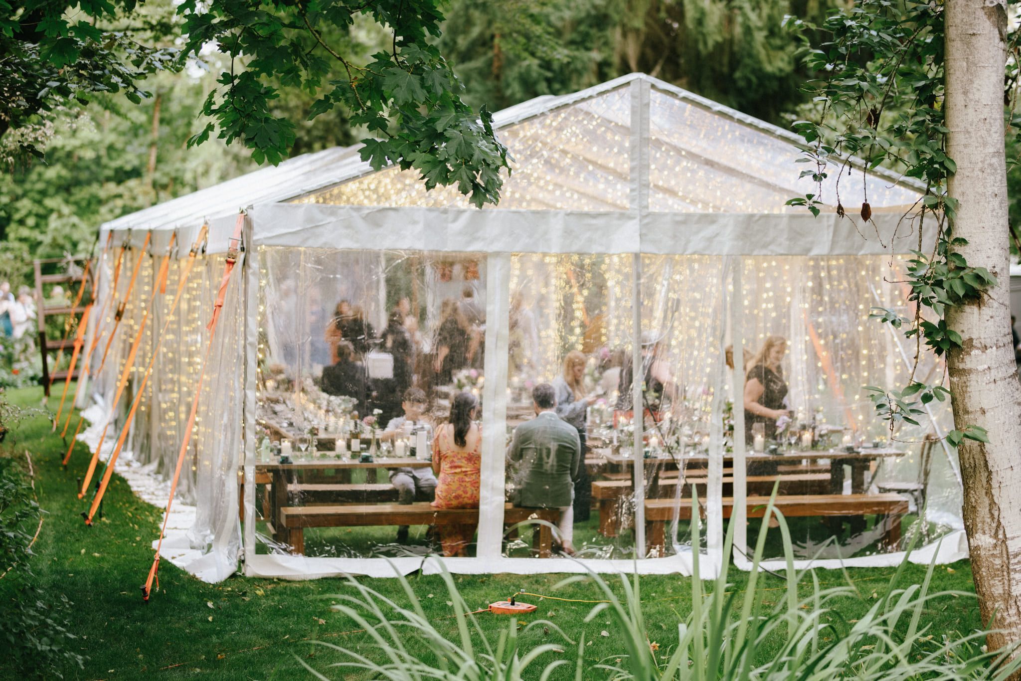 Simple wedding photoshoot, clear reception tent glowing with string lights in a forest clearing