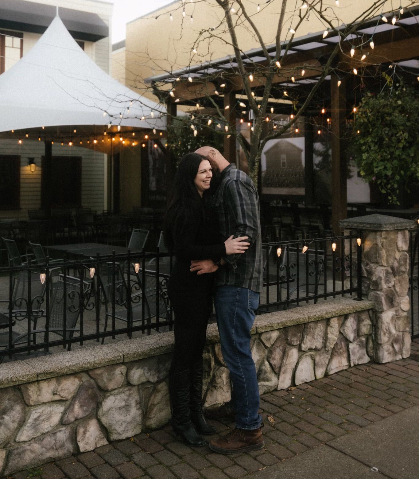 Couple embracing beside a patio strung with lights in Fort Langley village