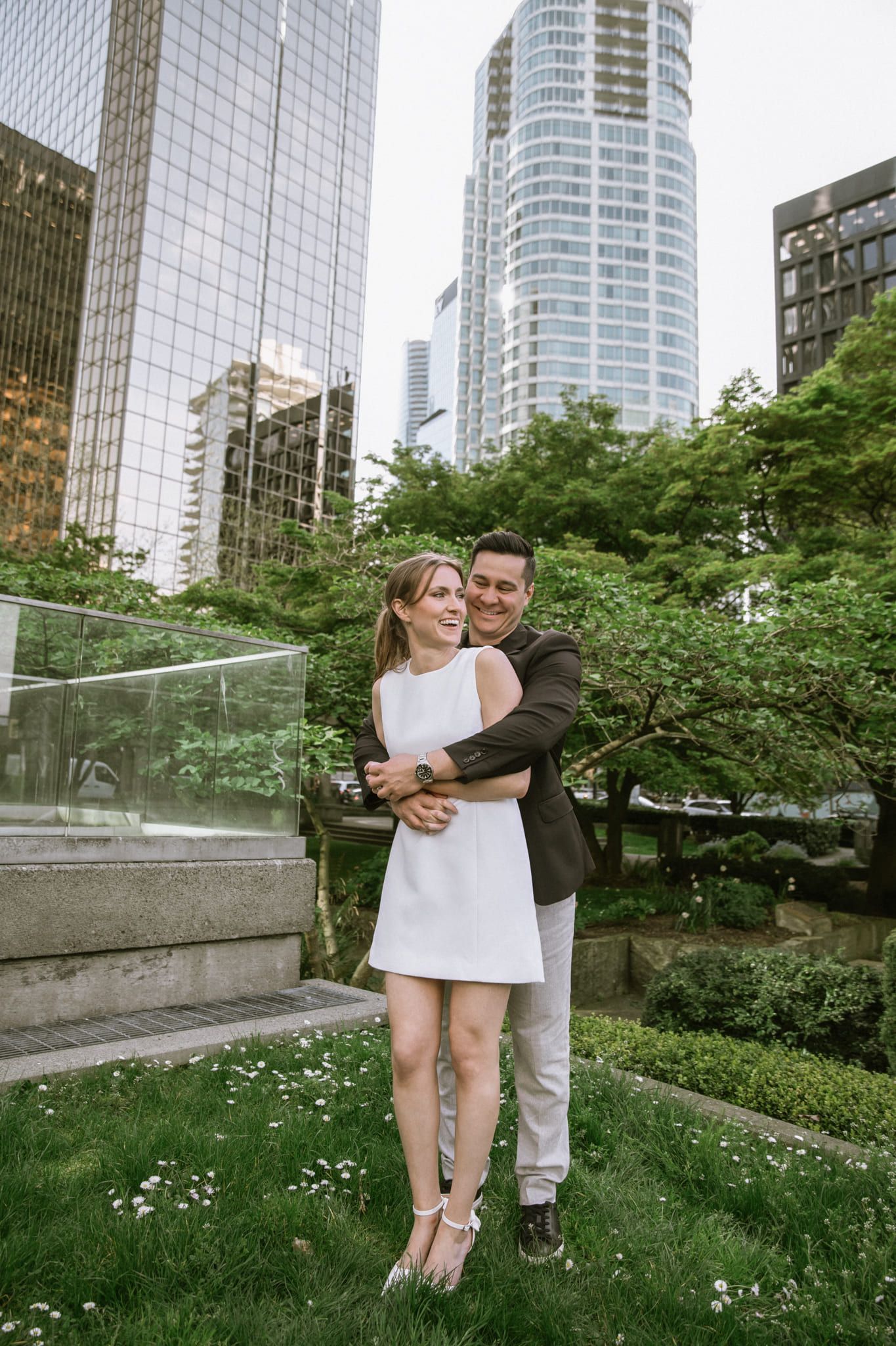 Wedding outdoor shoot below glass towers, couple hugging in a city garden