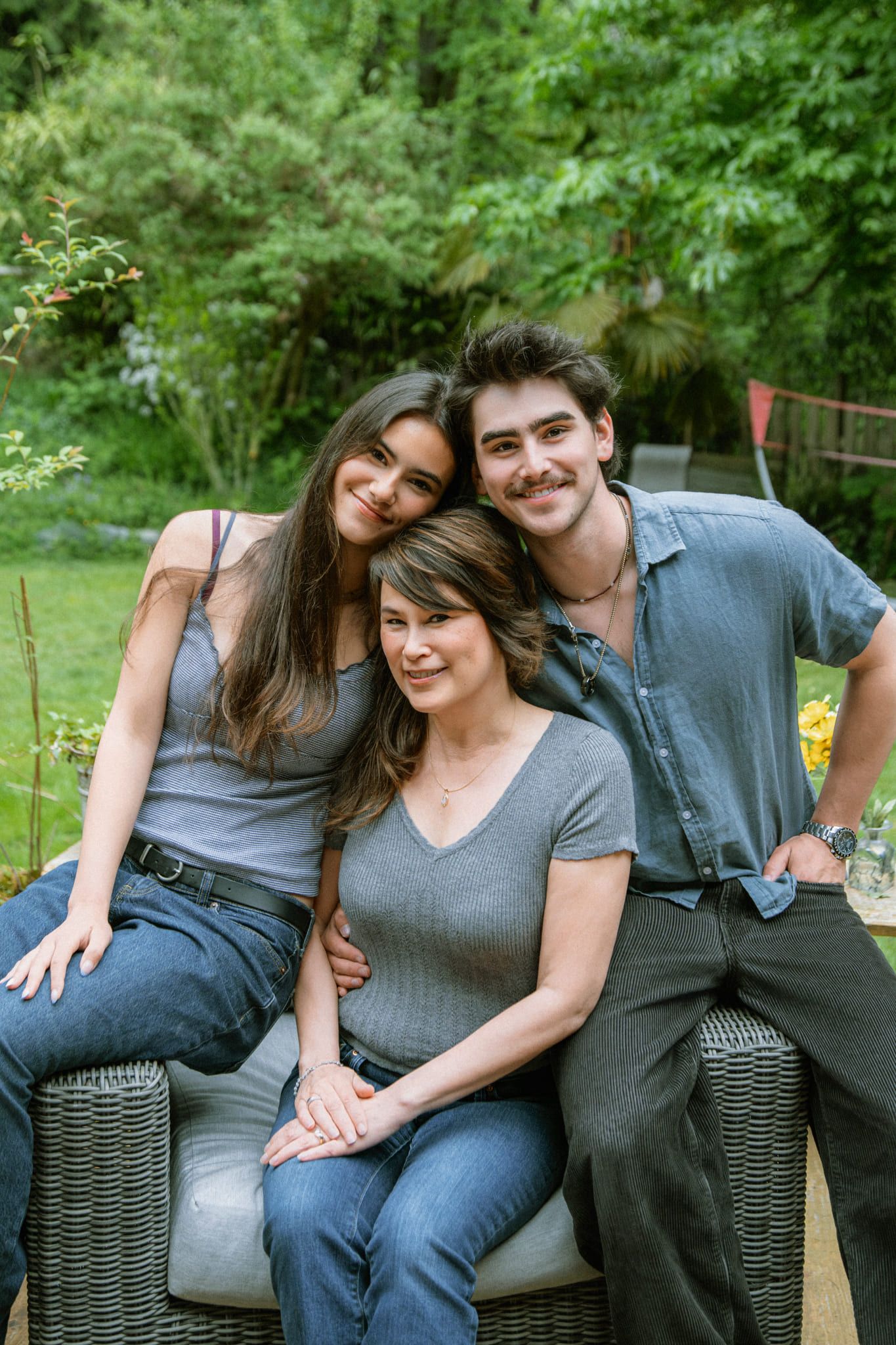 Family garden photoshoot, mother, son and daughter leaning in close on a garden chair