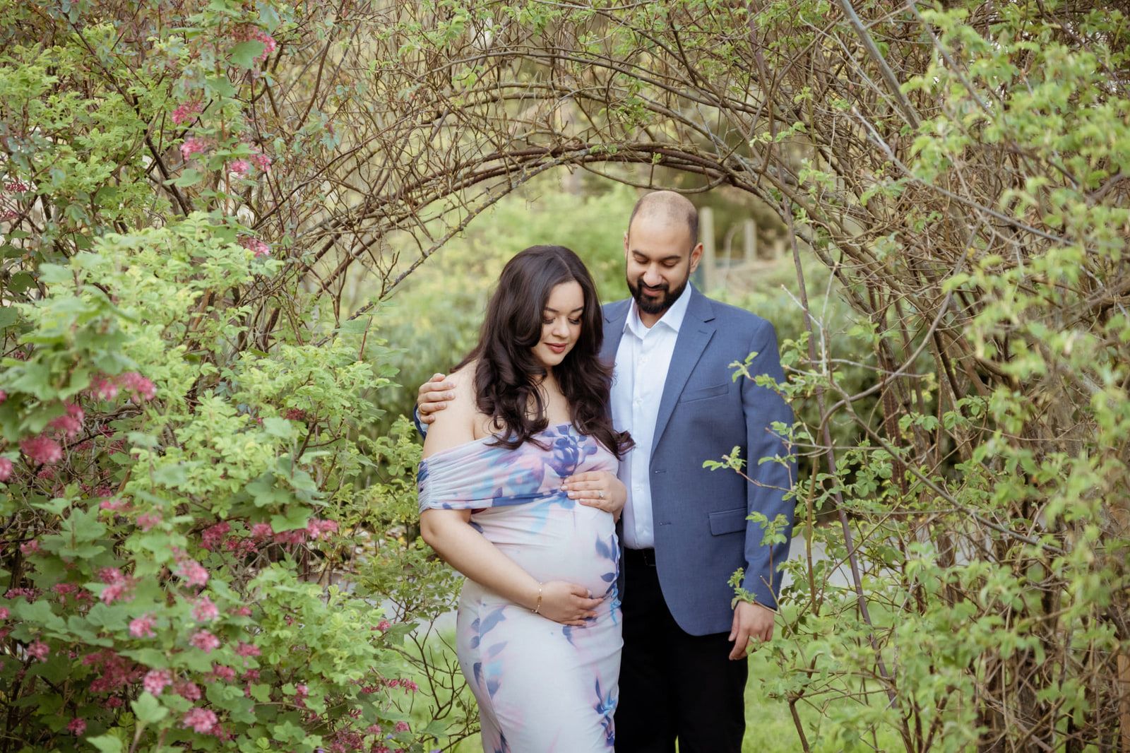 Intimate pregnancy photography in a garden, expecting couple under a flowering arch