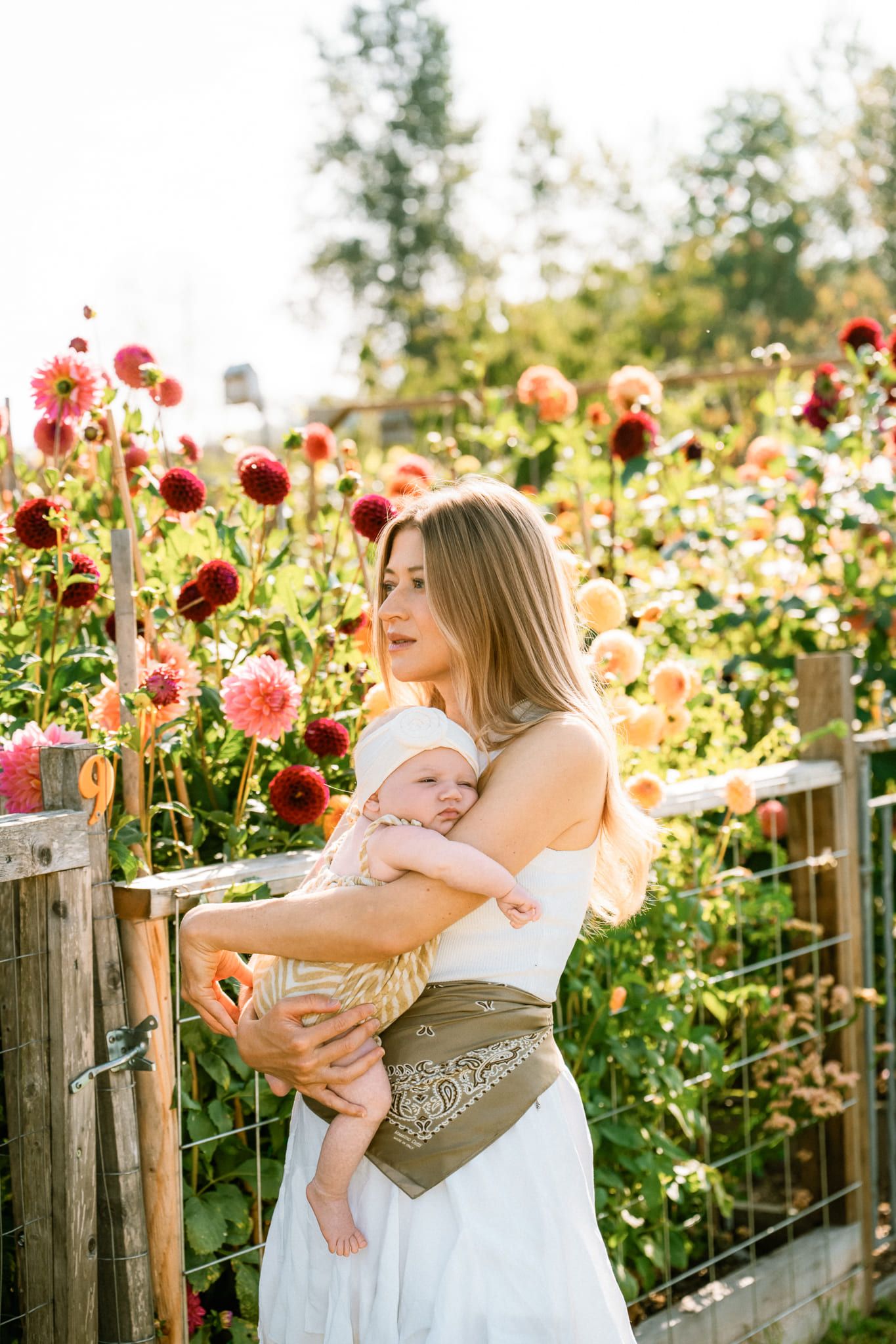 Newborn and mom photography in a sunny flower garden, mother holding her baby