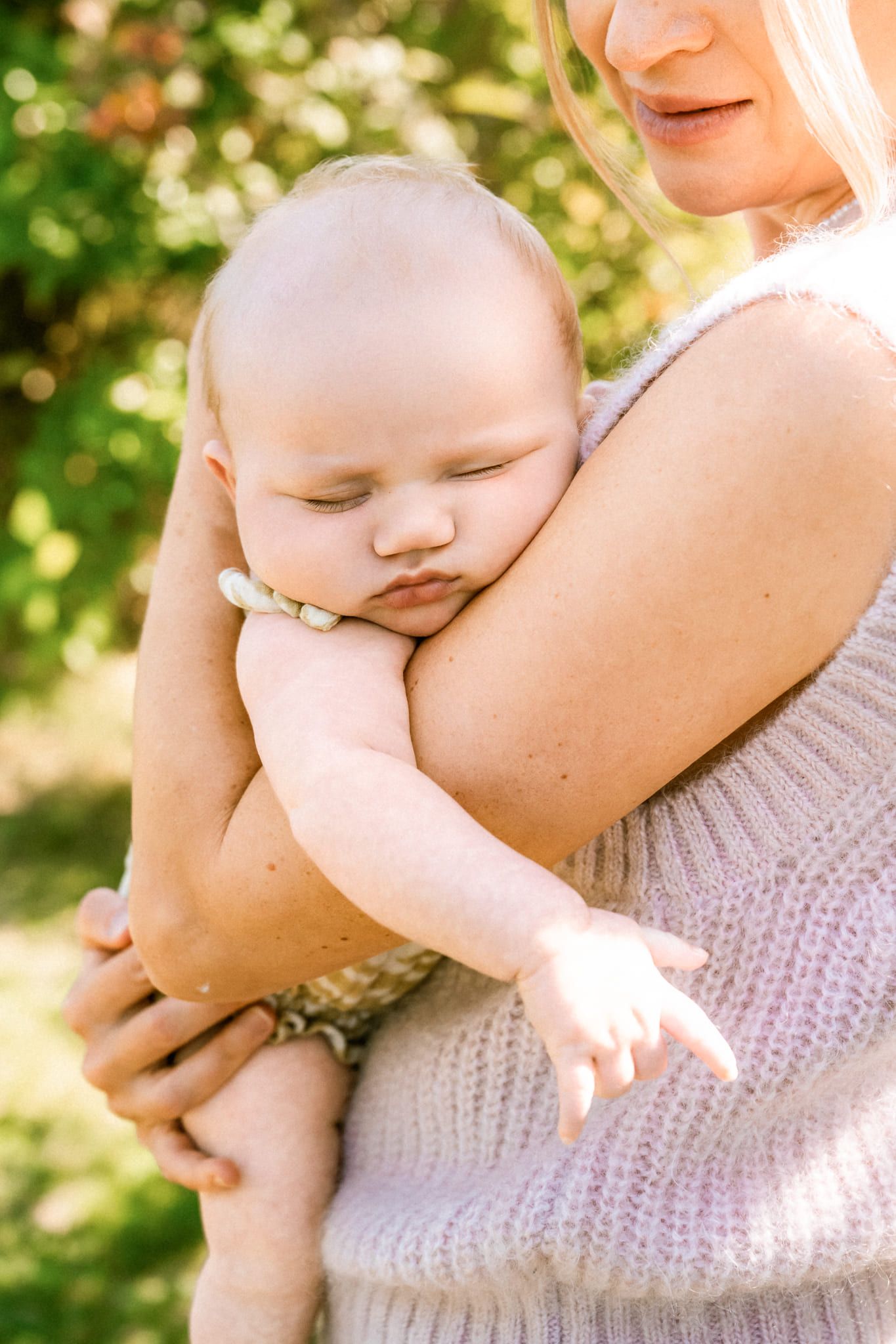 Mother and newborn photoshoot in a sunny garden, mom holding her sleeping baby