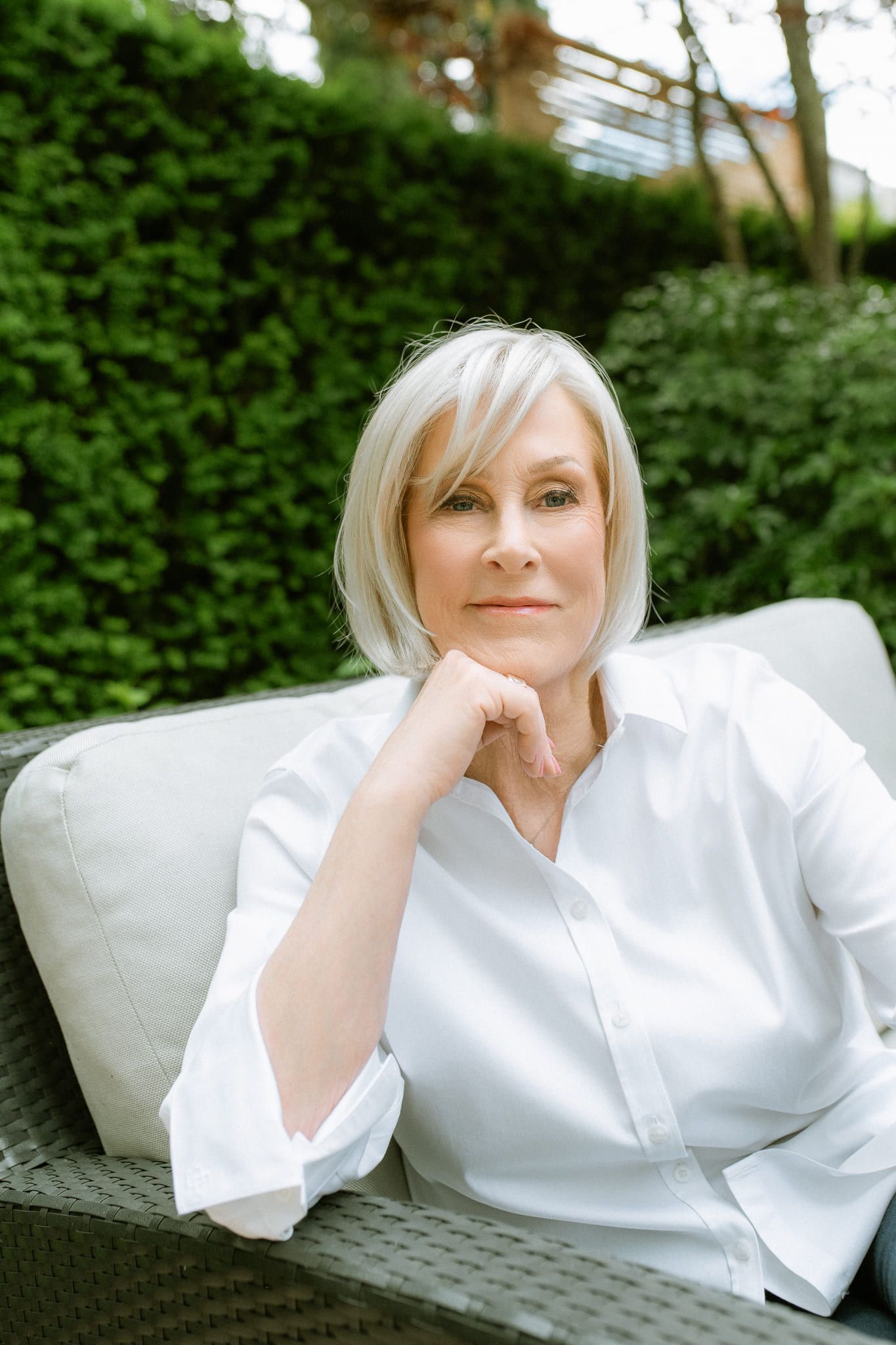 Professional portrait photo, woman with silver hair in a white shirt, relaxing in a garden chair