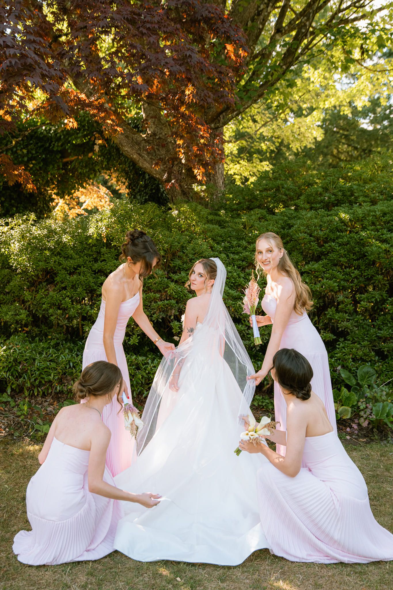 Outdoor wedding photography in a garden, bridesmaids in lilac fixing the bride's veil