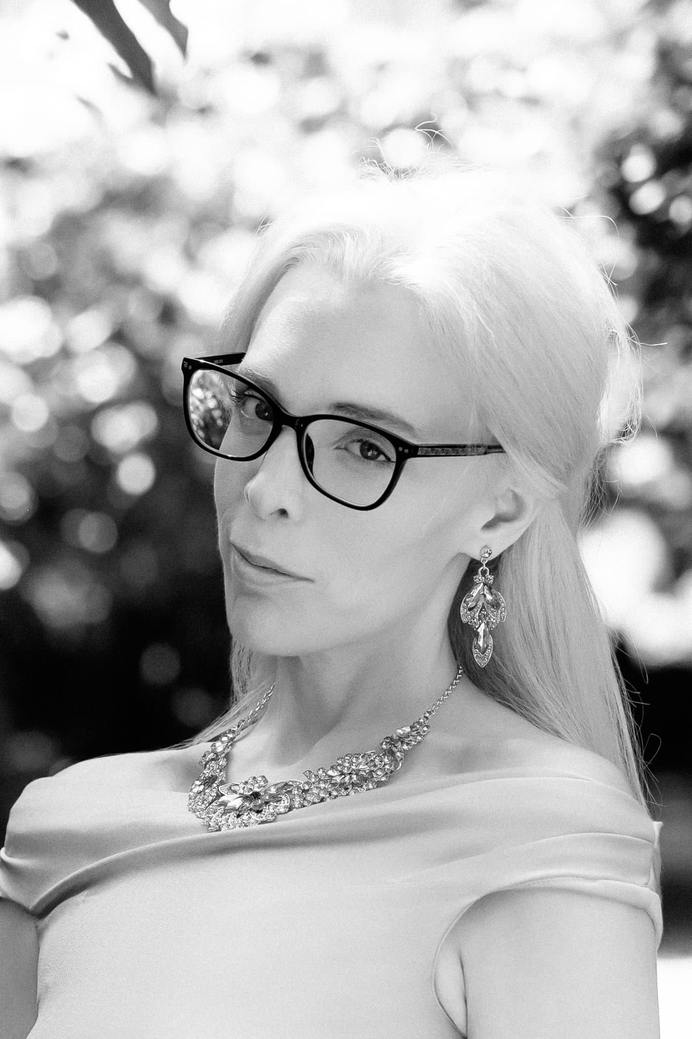 Monochrome portrait photography in a greenhouse garden, woman in a lilac dress and glasses, in black and white
