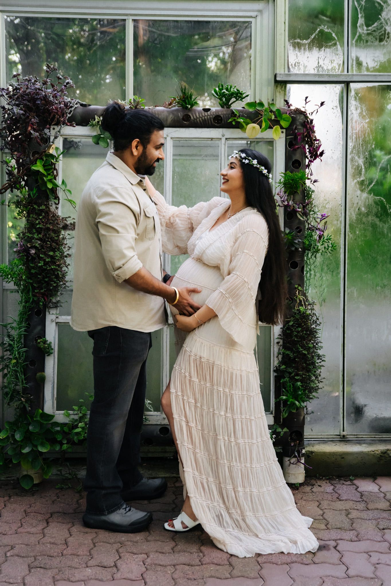 Garden maternity shoot, expecting couple holding hands in a garden glasshouse