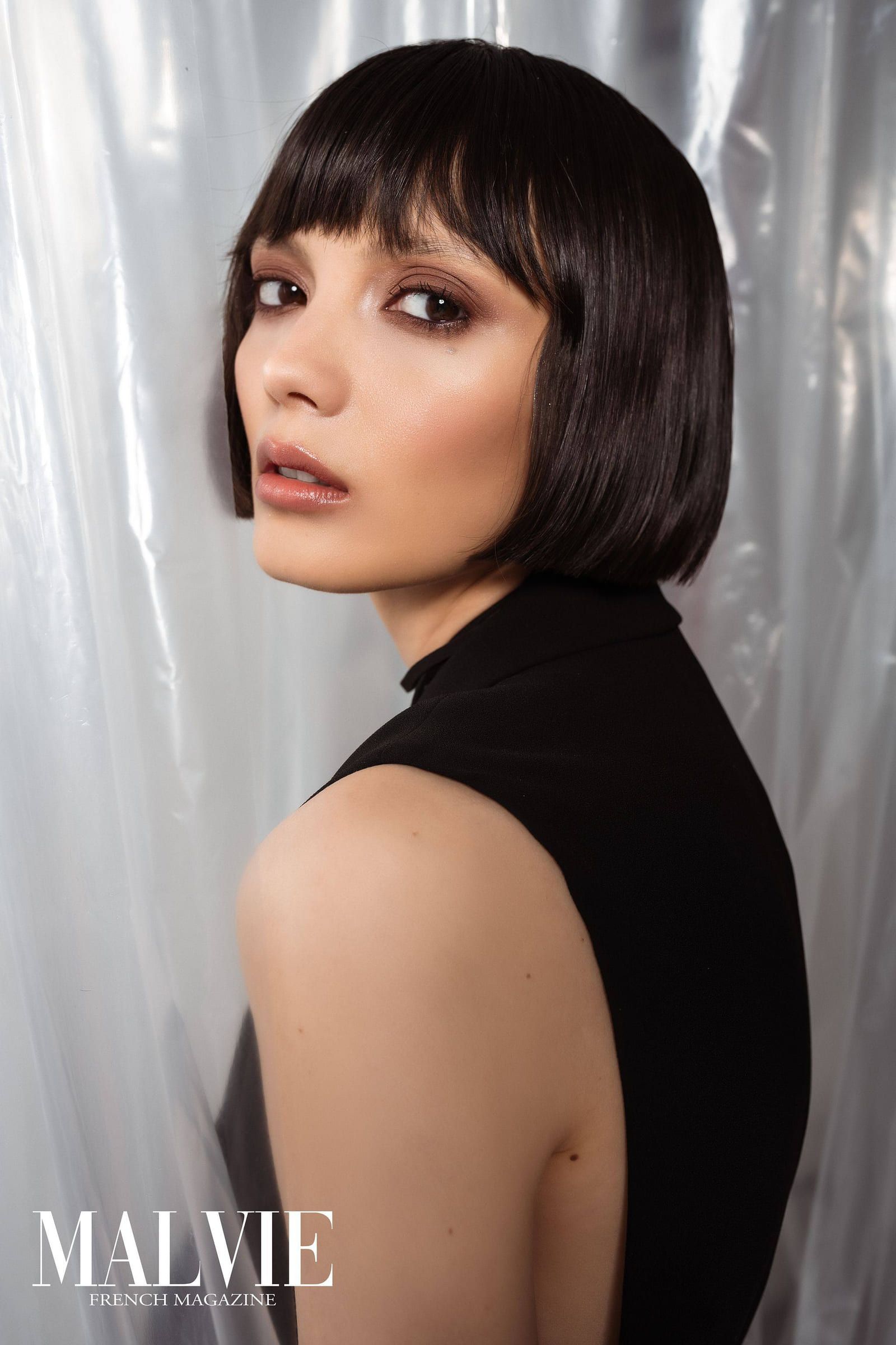 Model with a dark bob looking over her shoulder against plastic sheeting