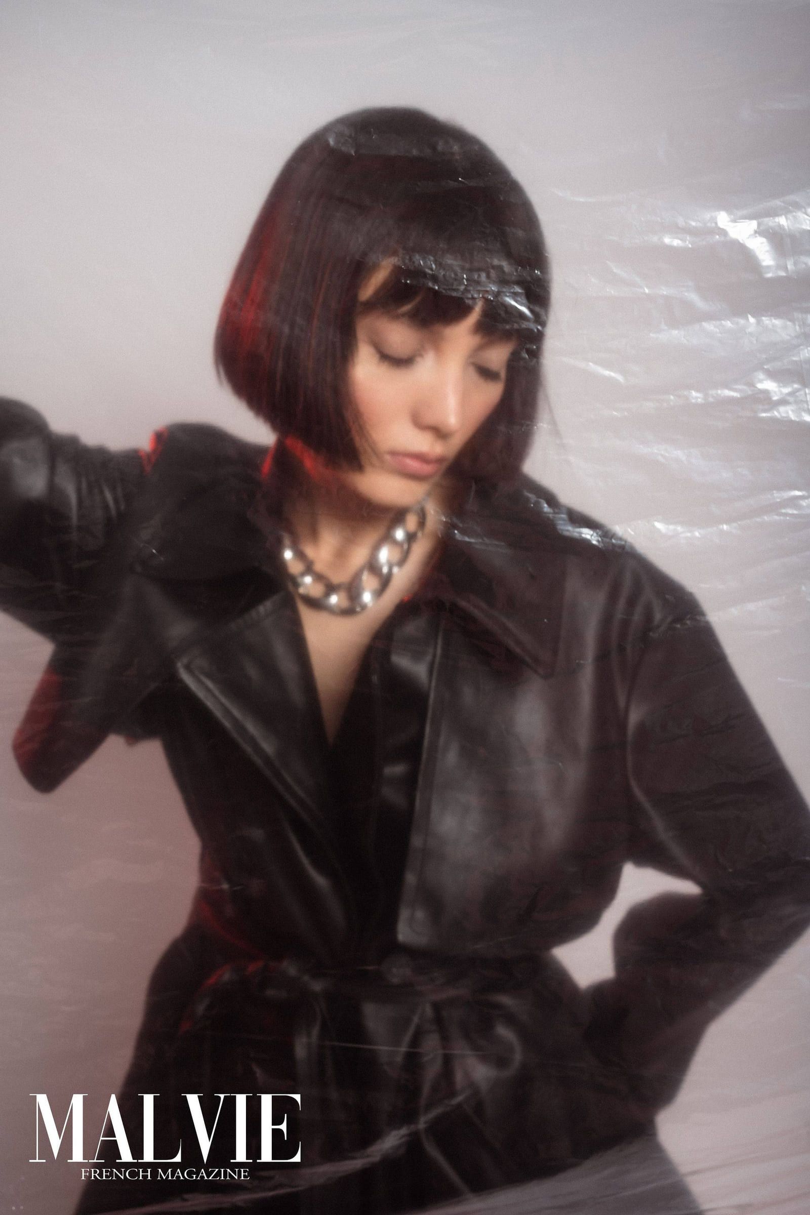 Model in a black leather coat seated among plastic sheeting