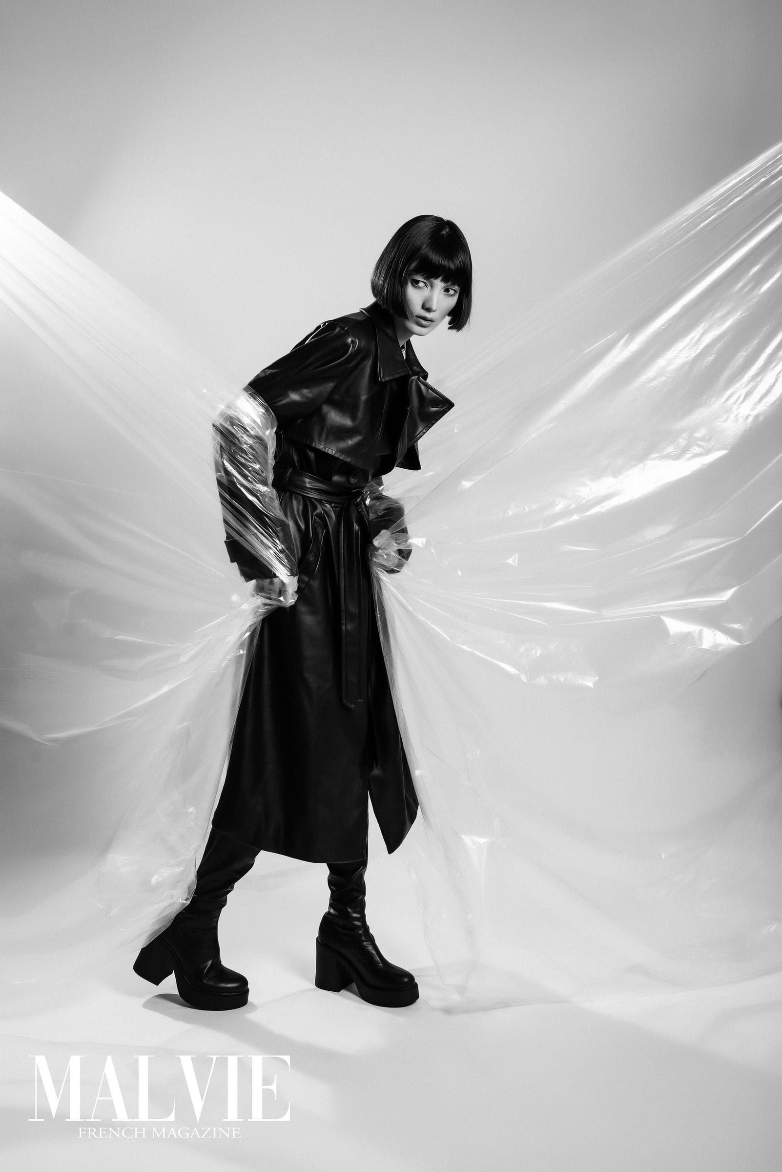 Black-and-white photo of a model in black leaning into plastic sheeting