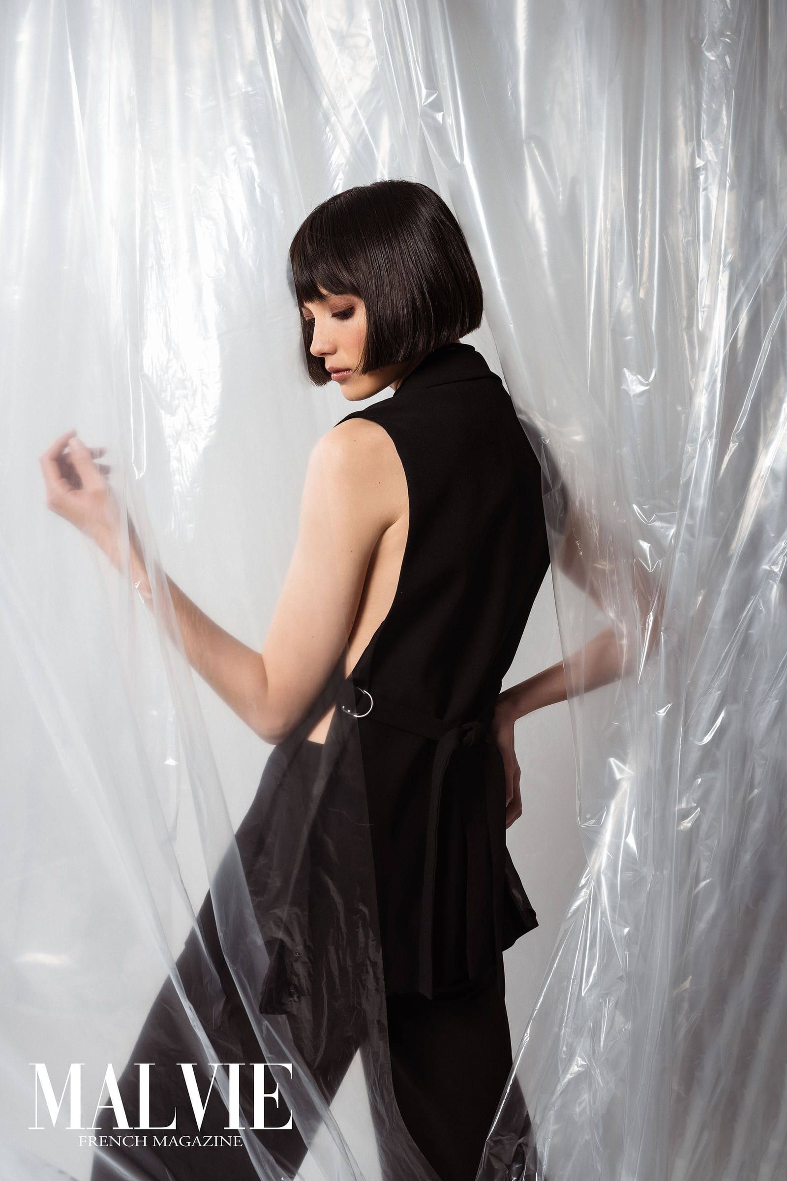 Model in black posing against a wall of clear plastic sheeting